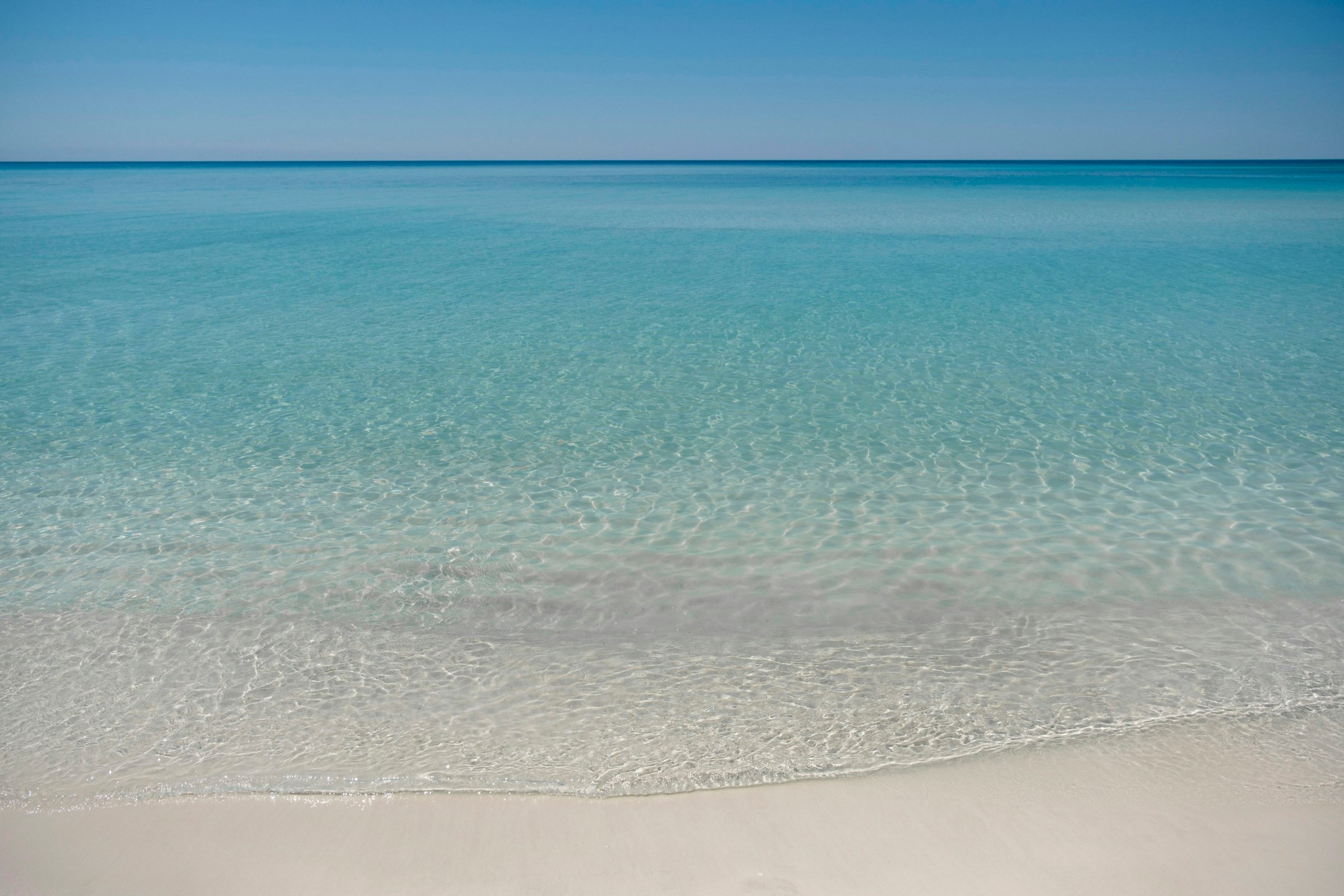 Emerald green Gulf water and white sand at a quiet beach access on the west end of Panama City Beach, Florida, on a clear summer morning