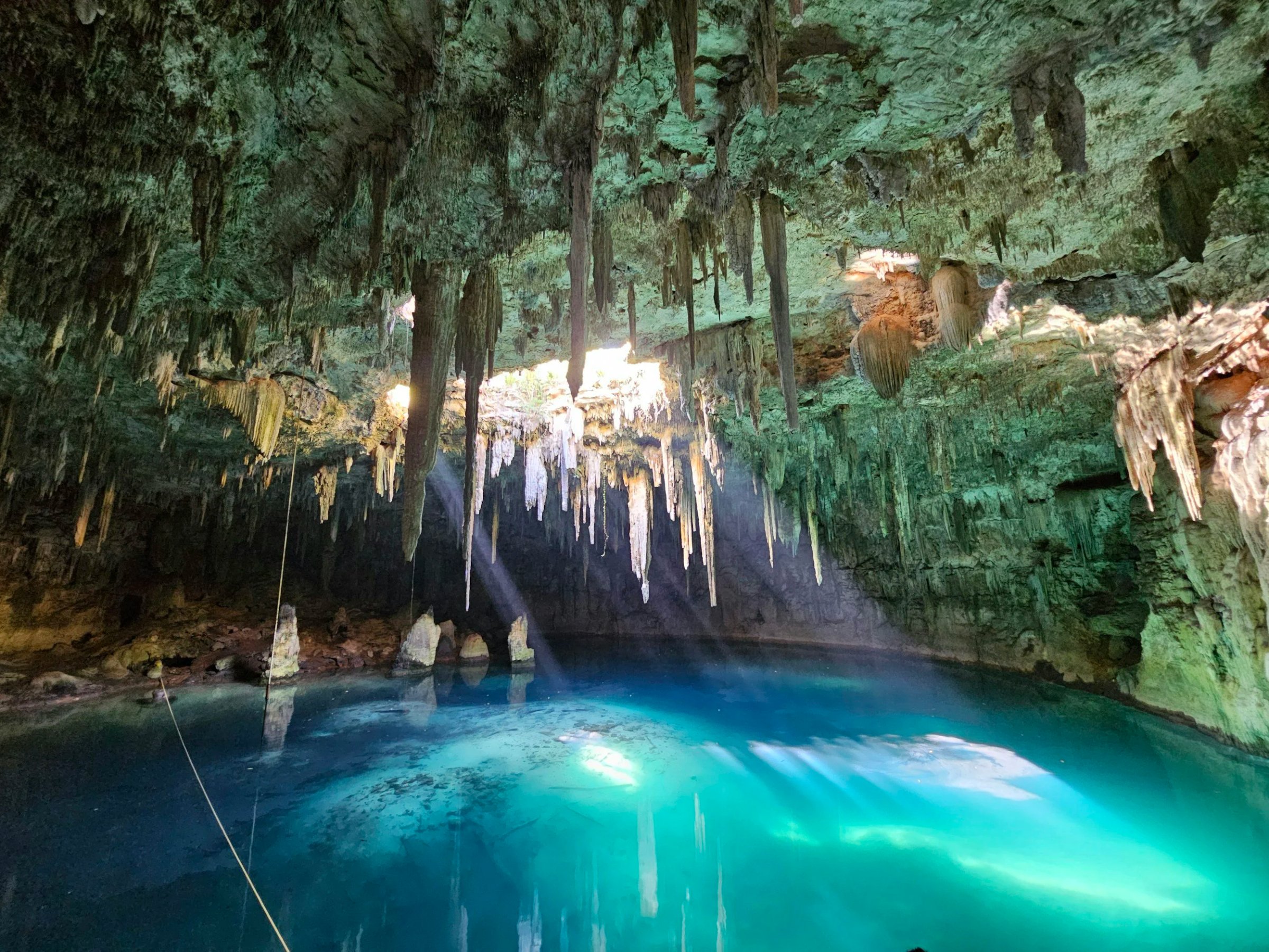 Inside a cave with stalactites hanging from the ceiling and a blue underground lake reflecting light.