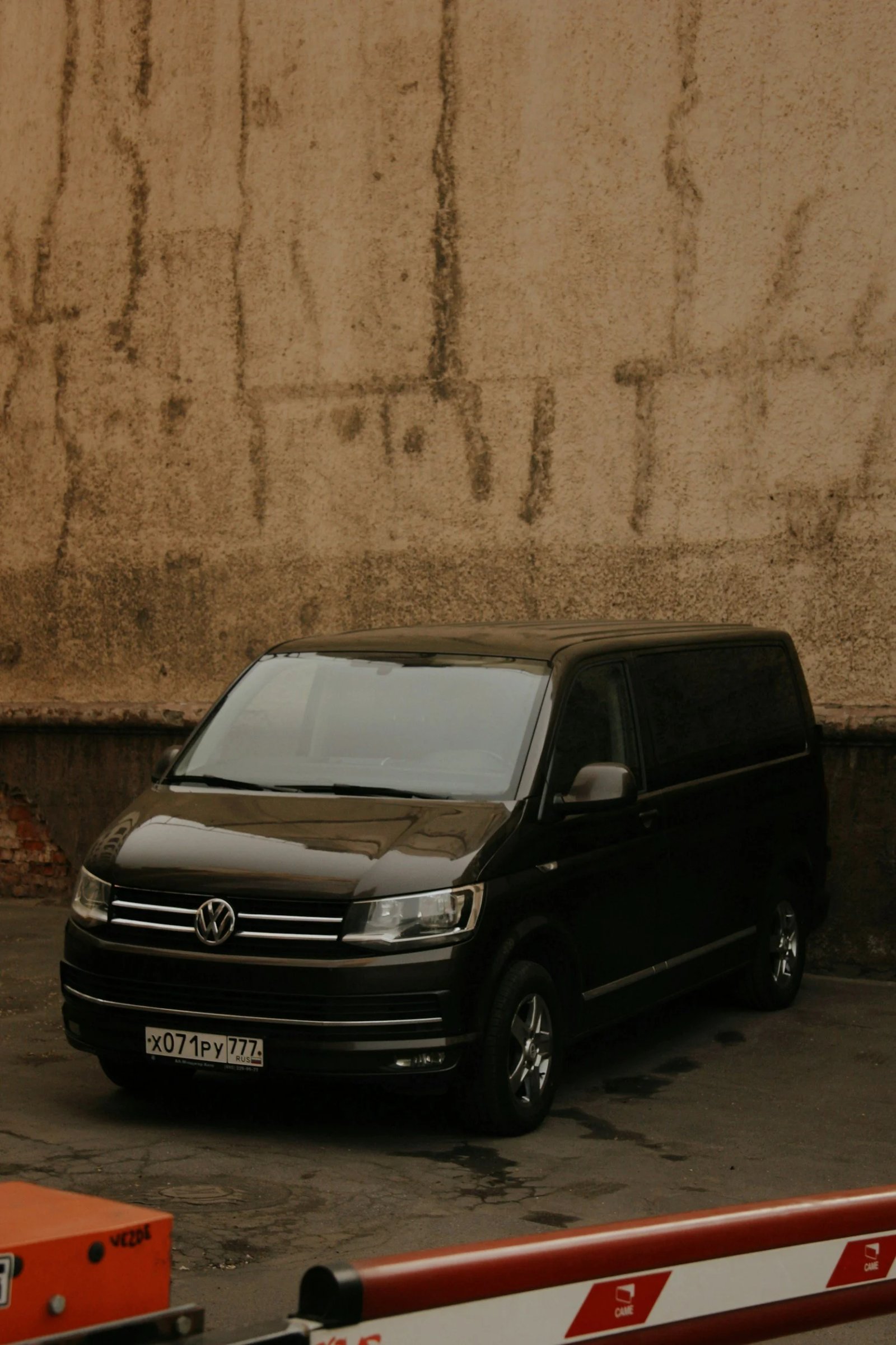 Black Volkswagen van parked against a beige brick wall in an outdoor lot.