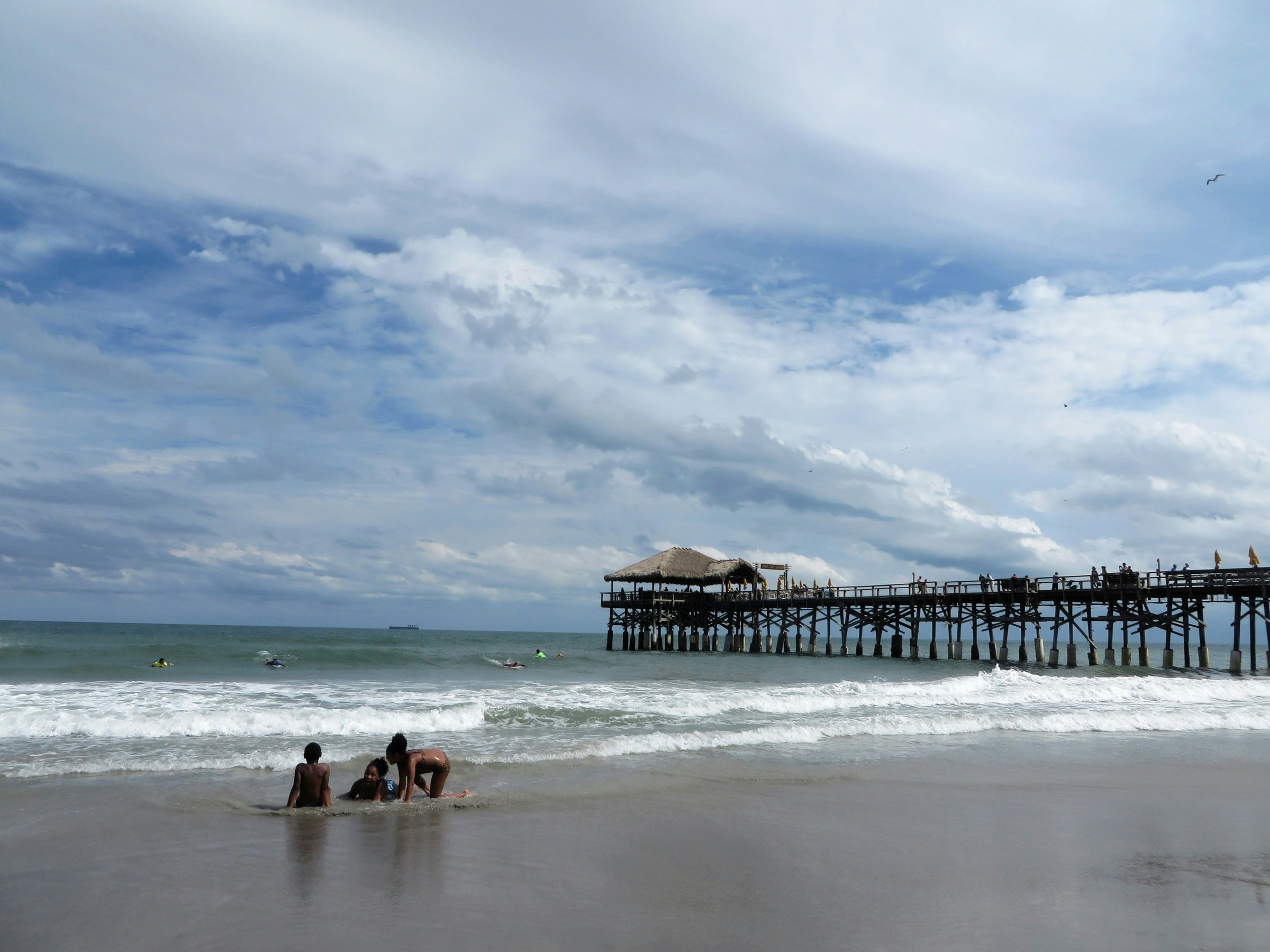 Morning surfers walking down the sand at Cocoa Beach, Florida, with the Cocoa Beach Pier in the distance