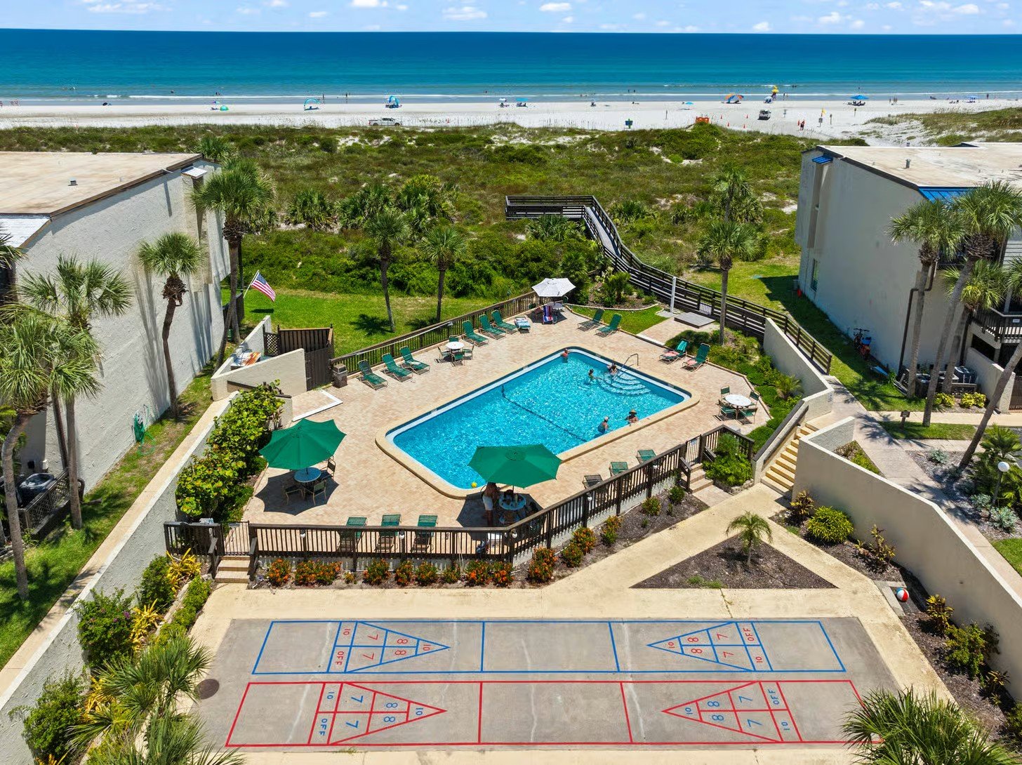 Aerial view of the Island House complex pool with shuffleboard courts, palm trees and the beach directly behind it