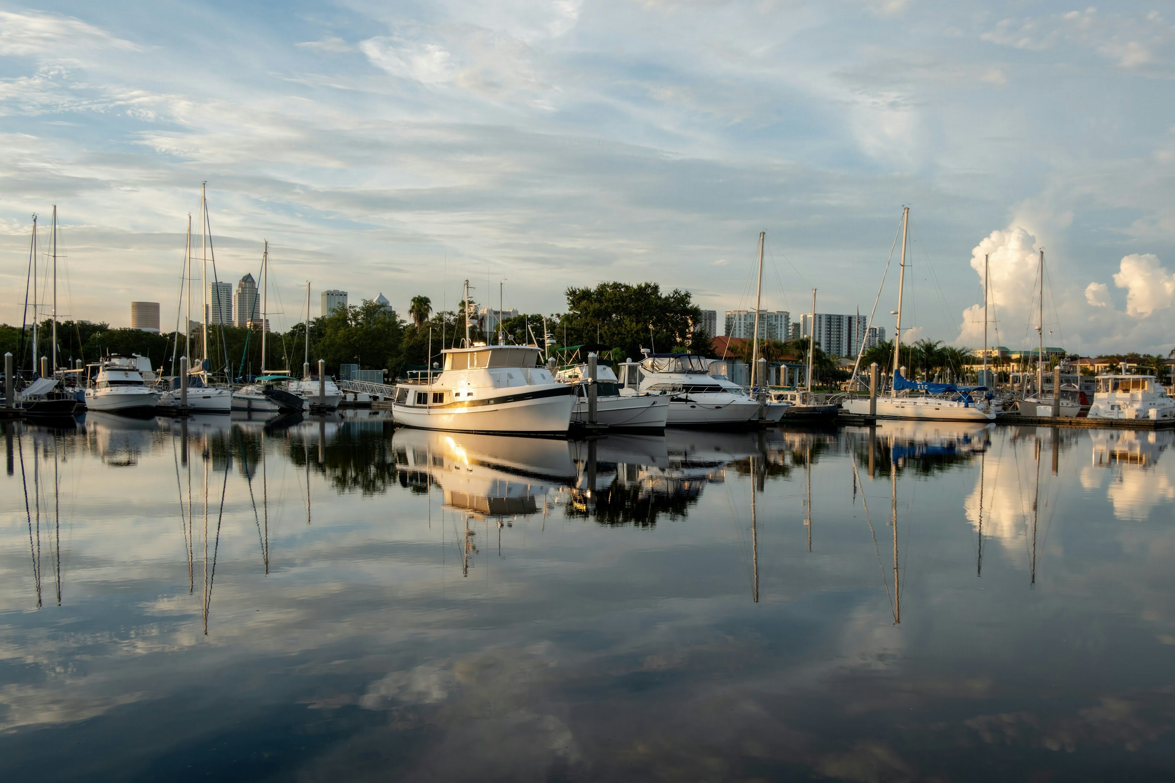 Sailboats and yachts docked in a calm harbor with the Saint Petersburg, Florida skyline reflected in the water