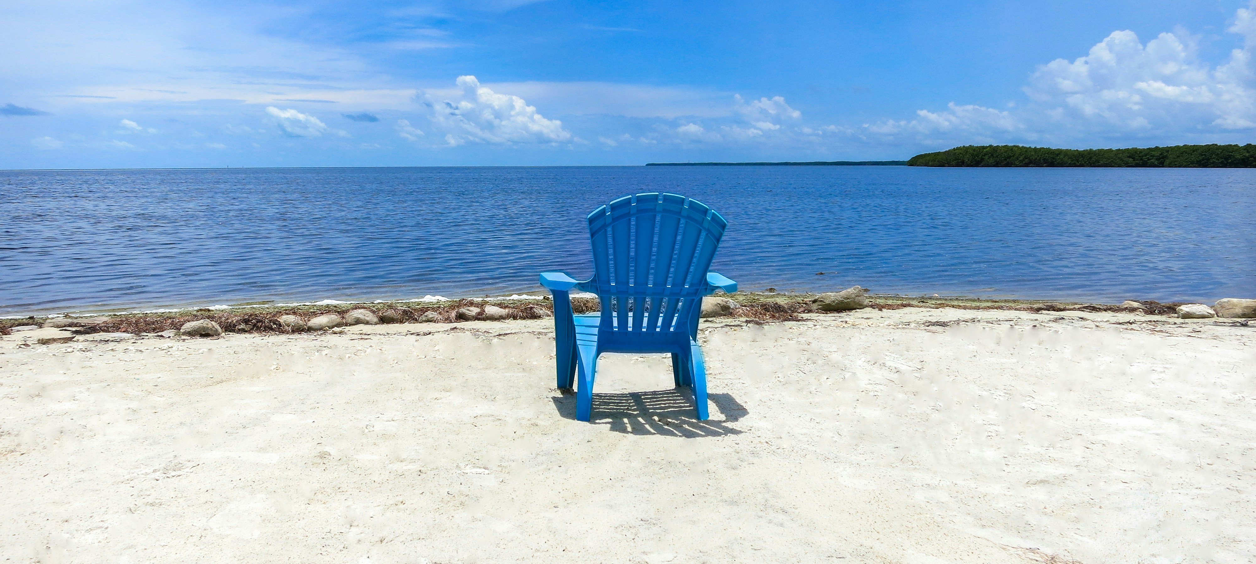 Blue Adirondack chair on a quiet white sand beach with calm turquoise water, Anna Maria Island, Florida