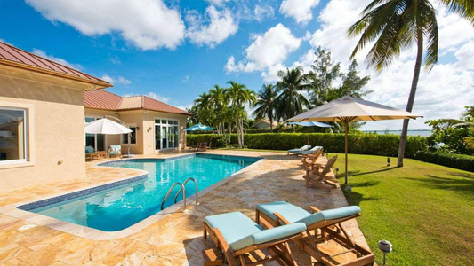 A luxury villa's pool with lounge chairs and palm trees in the background on a clear bright day in Grand Cayman in a Spanish style villa