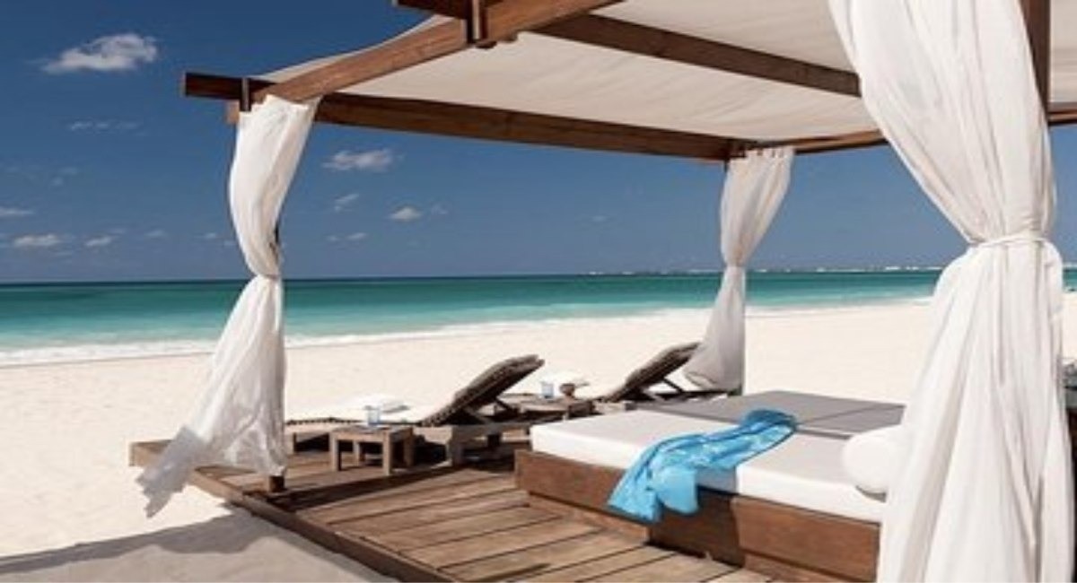 Luxury beach cabana with white drapes and sun loungers overlooking a white sand beach and turquoise sea in Grand Cayman