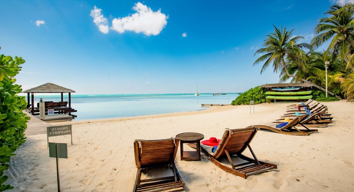waterfront view of the beach with lounge chairs and tables overlooking turquoise water and a gazebo in the distance