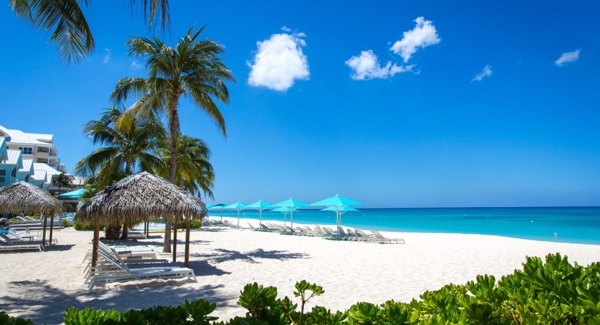 Seven Mile Beach Grand Cayman's silky white sand with turquoise Caribbean water, palm trees, and beach chairs under umbrellas