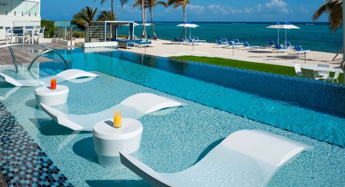 Club Suites at Rum Point infinity pool with white floating lounge chairs overlooking crystal-clear Caribbean waters and pristine Grand Cayman North Side beach