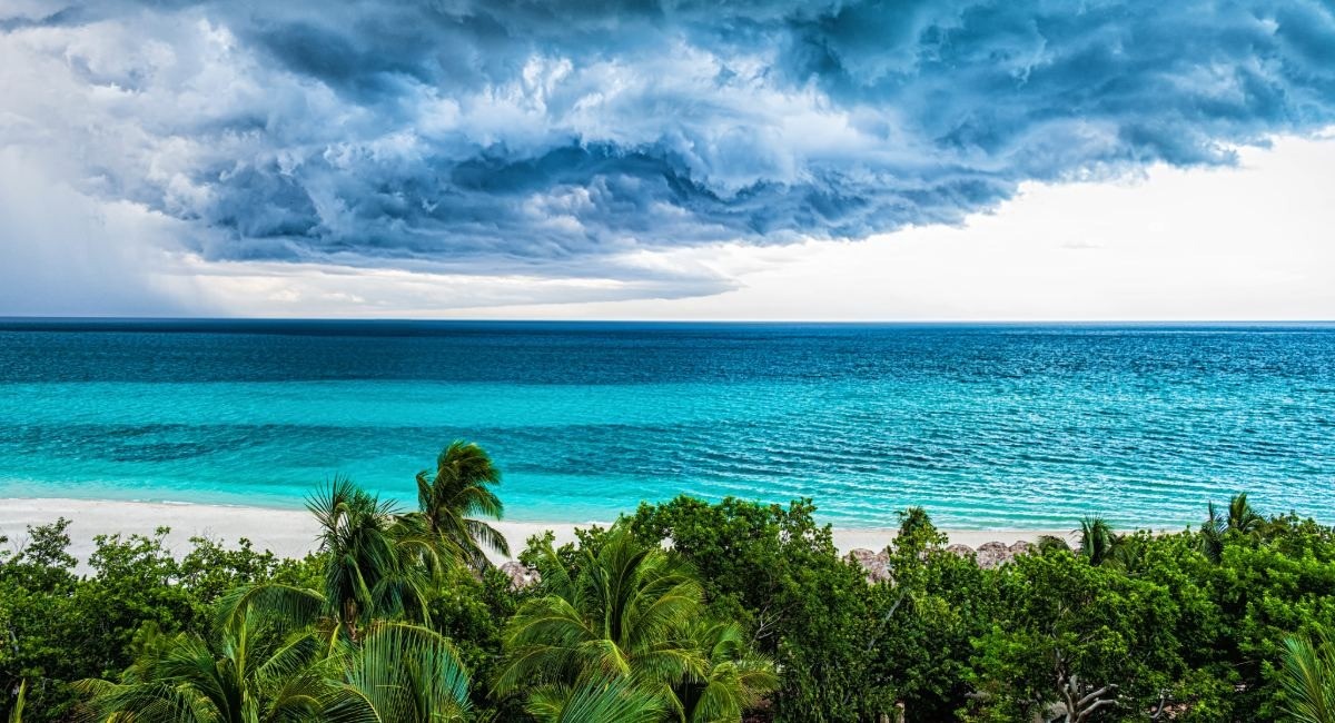 Dramatic tropical storm clouds looming over a pristine turquoise ocean and lush green coastline, illustrating Caribbean hurricane season weather