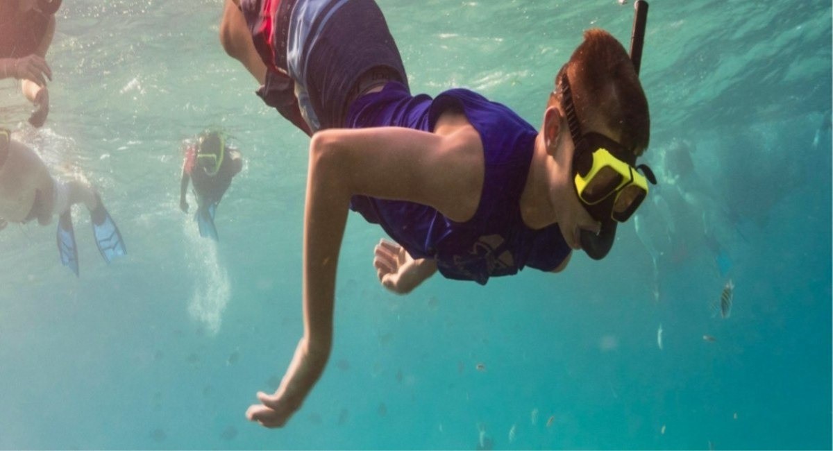 Young snorkeller diving underwater among fish in the clear turquoise waters of Grand Cayman