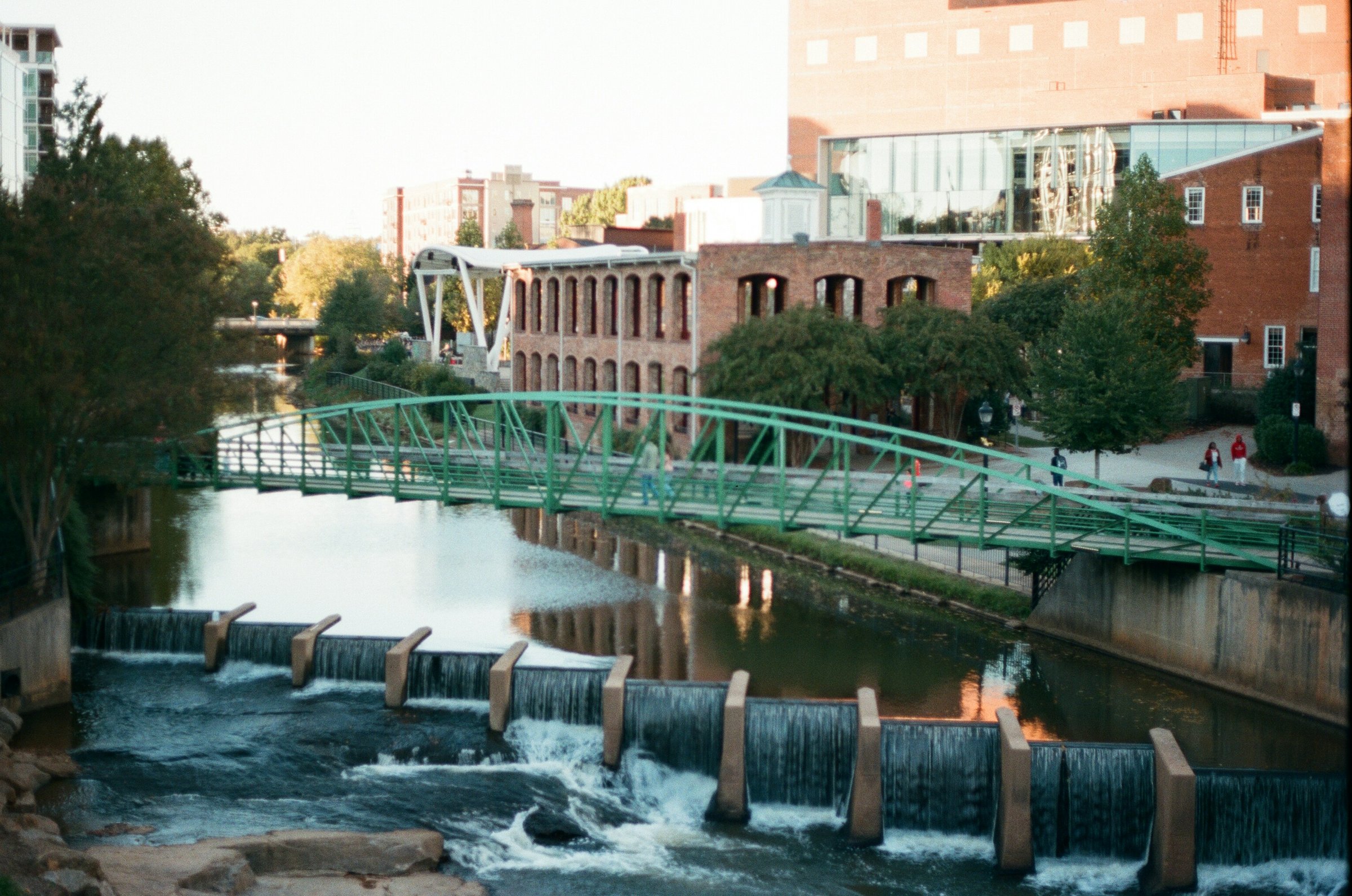 Walkers crossing the curved Liberty Bridge above the Reedy River falls in Greenville's West End