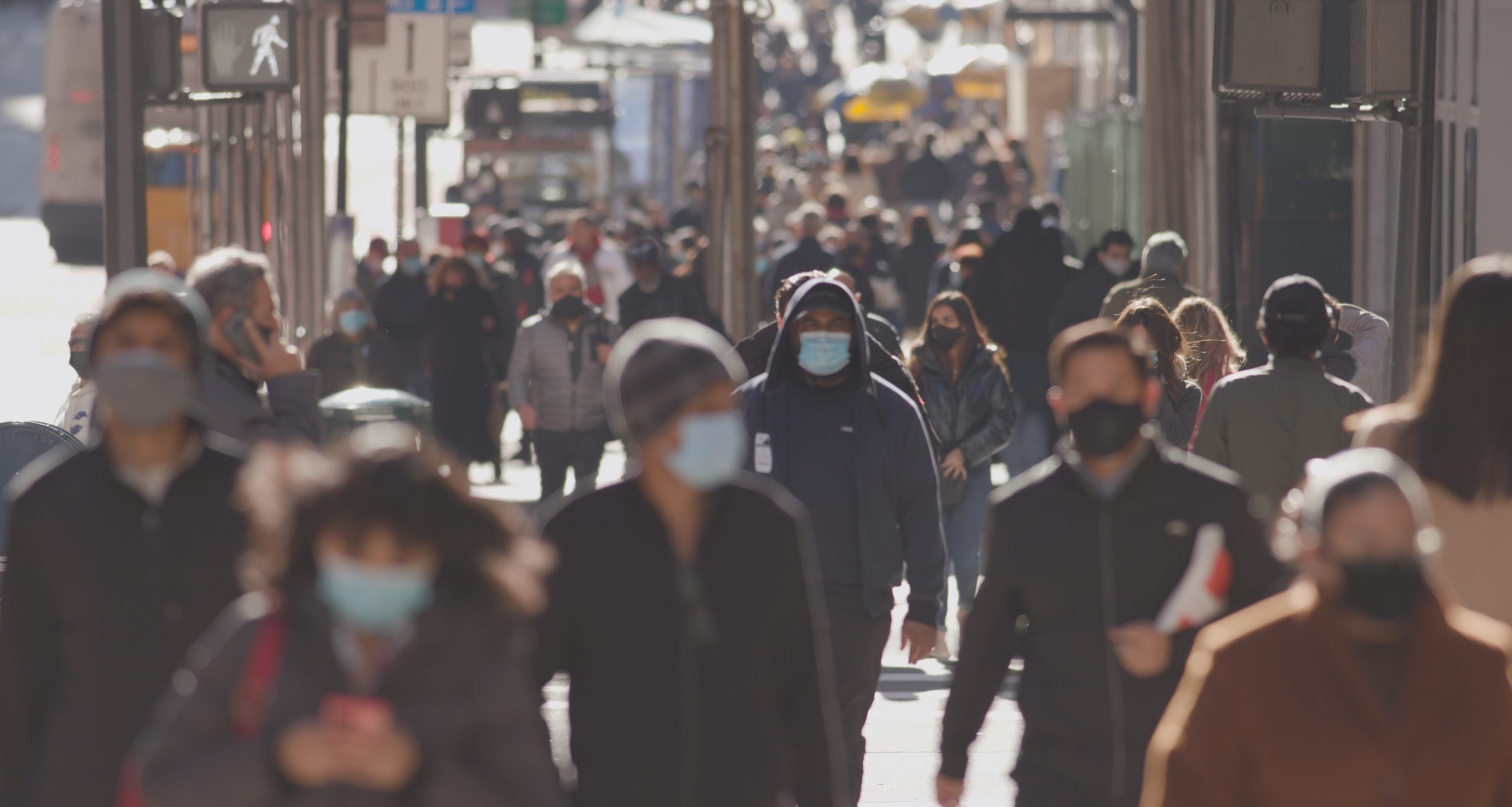 Crowd of people walking street wearing masks