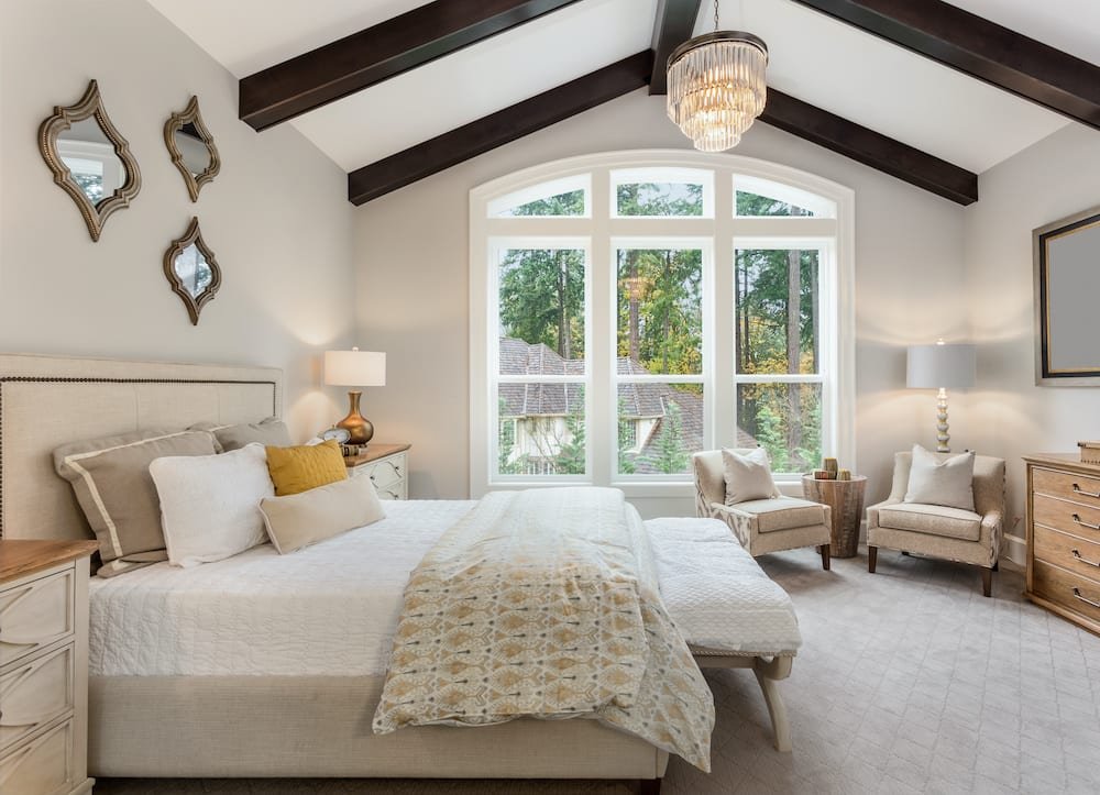 An extended stay housing bedroom waits for its next visitor. High ceilings, big windows, and a nice bed decorate the room.