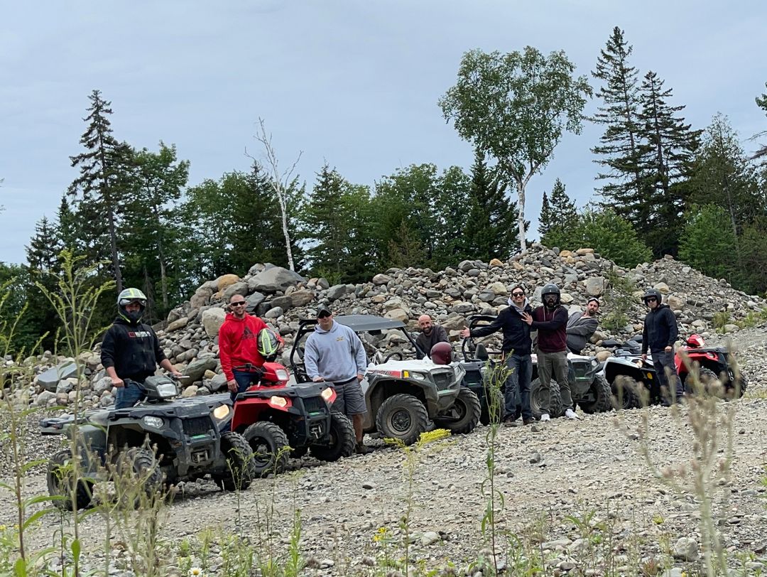 Group of people with ATVs on a rocky trail surrounded by trees.