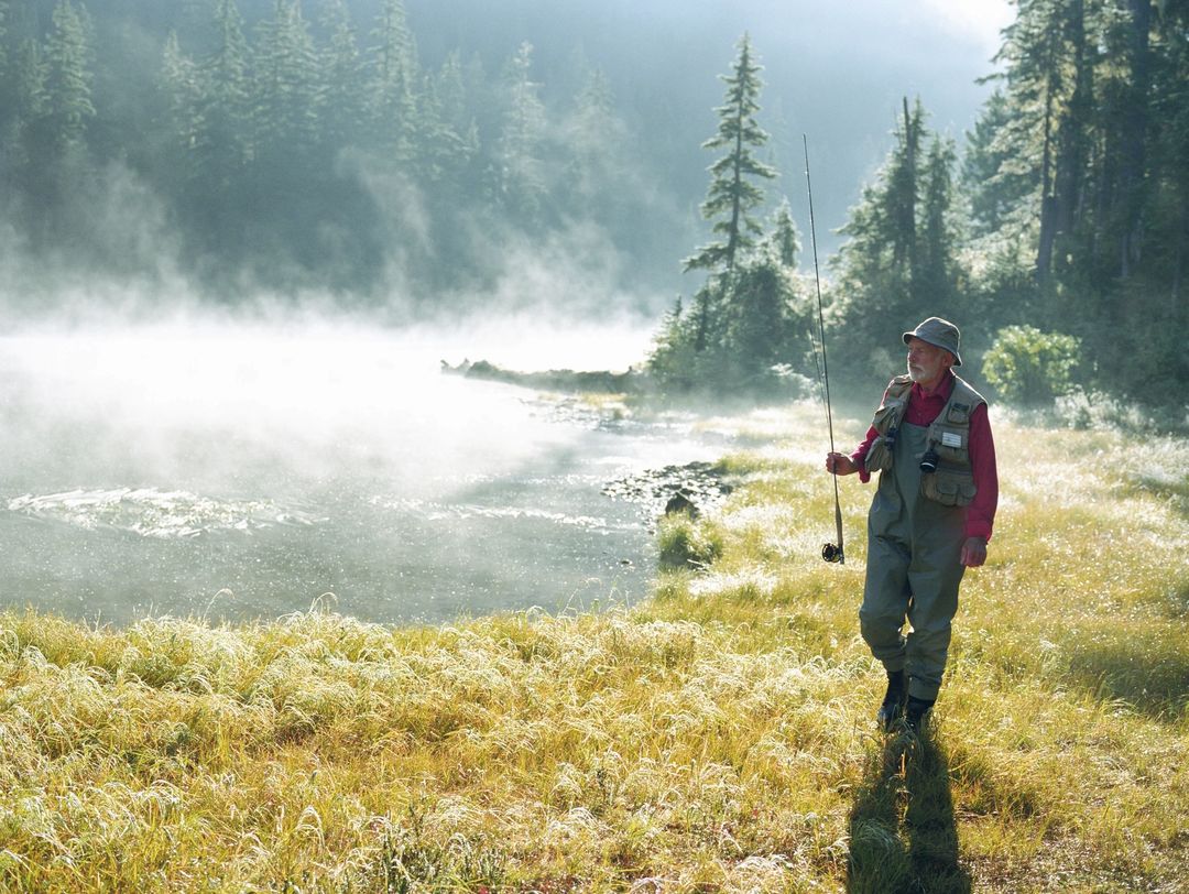 A person fishing near a misty river surrounded by trees.