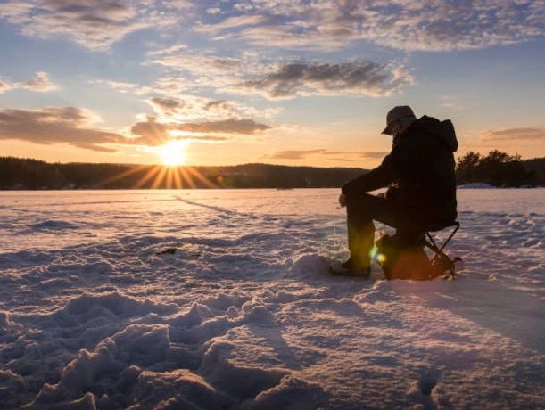 Person ice fishing at sunset on a frozen lake.