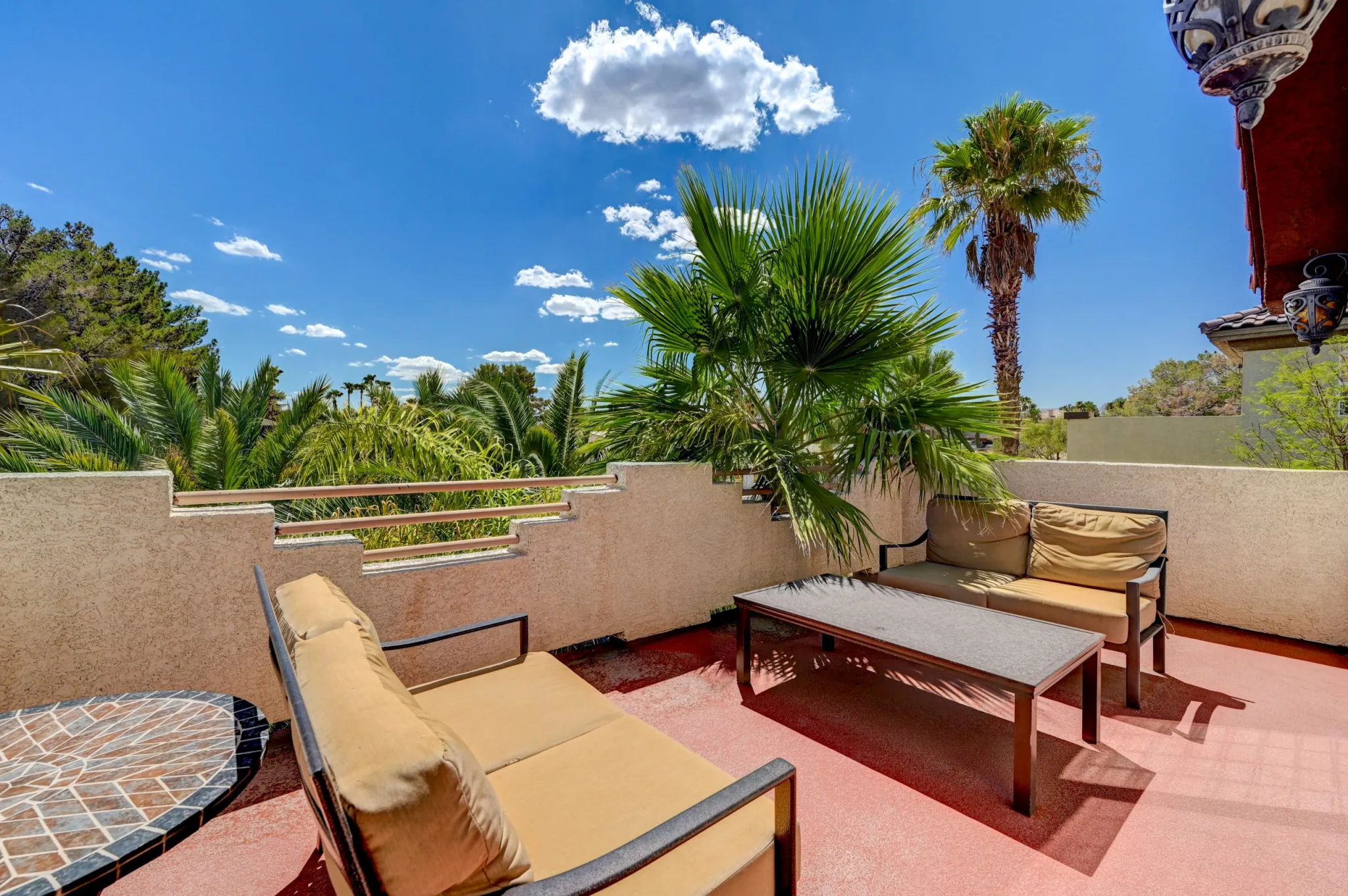 The upstairs patio at Paradise Estate with two outdoor sofas, a table, blue skies and palm trees all around
