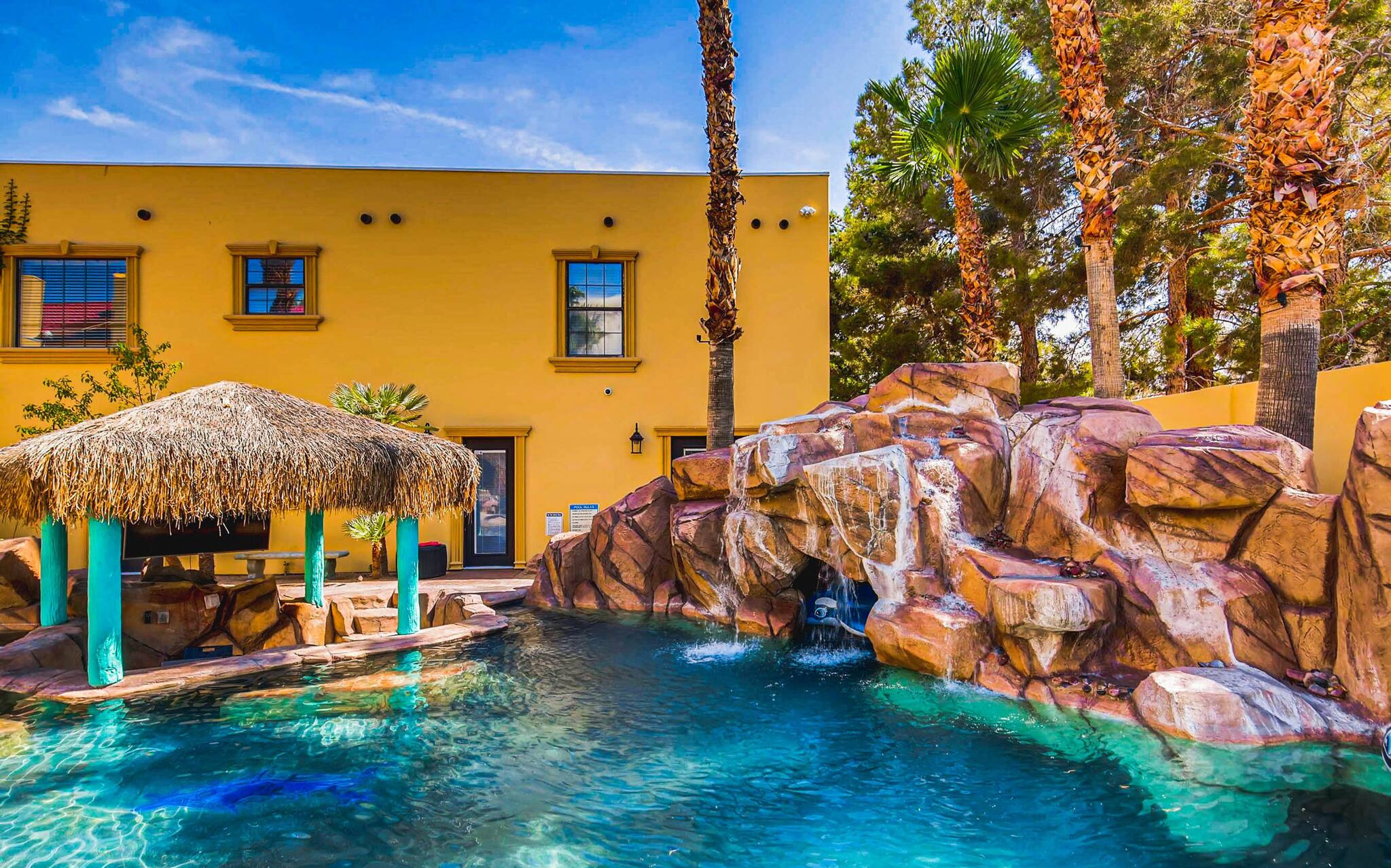 A bright yellow rental villa with a large resort-style pool, grotto and palapas, in Las Vegas.