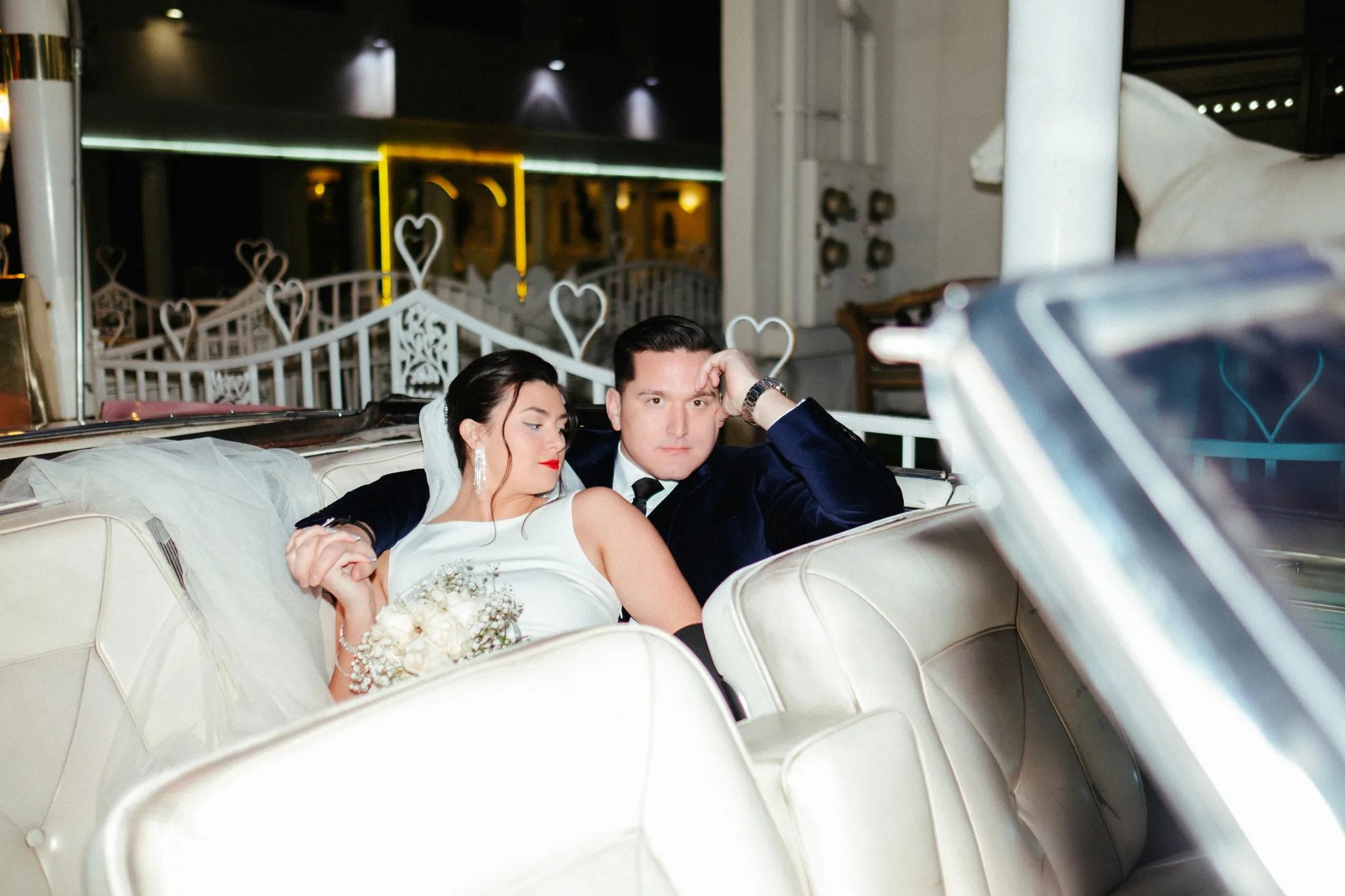 An elegant couple sit in the back of a convertible in wedding attire in Vegas