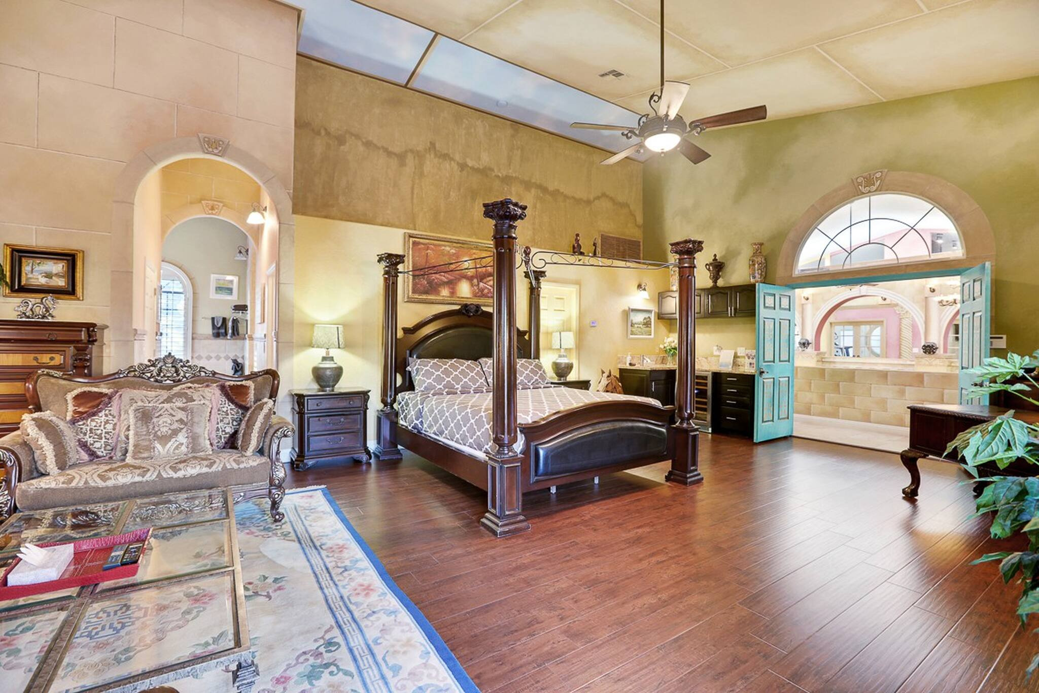 A grand master bedroom with high ceilings, stone walls, a half circle window over the door, and a 4-post wooden bed