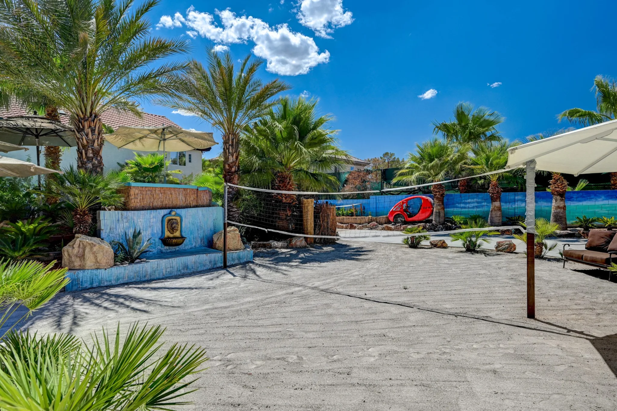A sandy volleyball course with palm trees and a villa in the backyard of Paradise Estate, a luxury villa in Vegas.