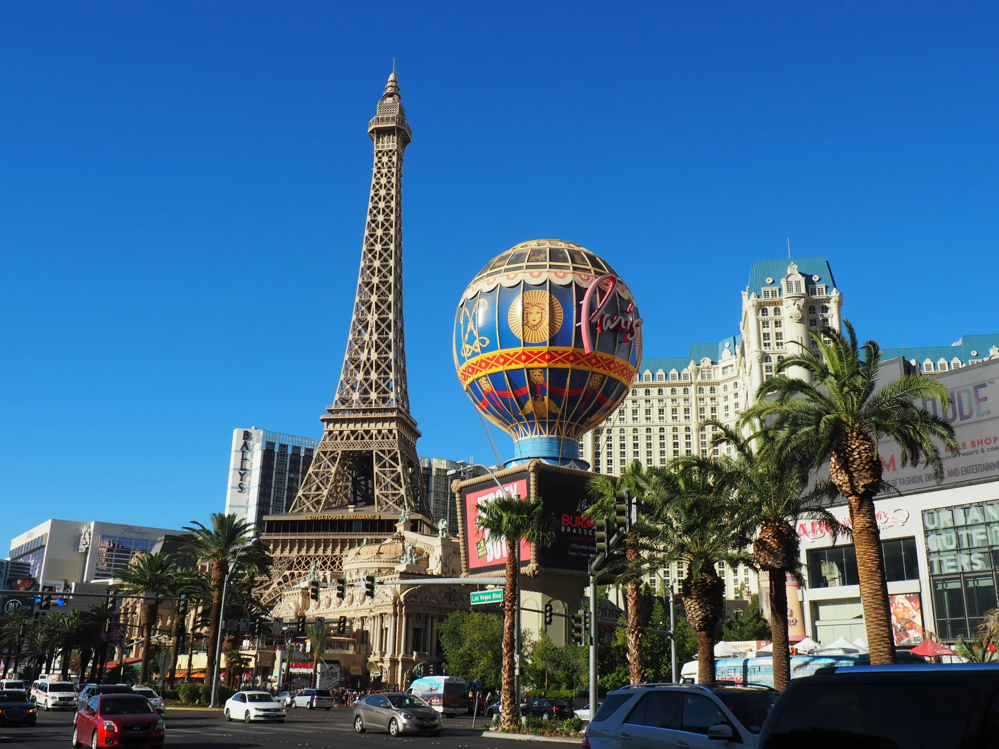 The Eiffel Tower at Paris Las Vegas is seen on a bright blue sky backdrop. It's a half-sized replica of its counterpart in Paris, neighboured by the Paris Las Vegas sign on a pretend hot air balloon, and with hotels in the background.