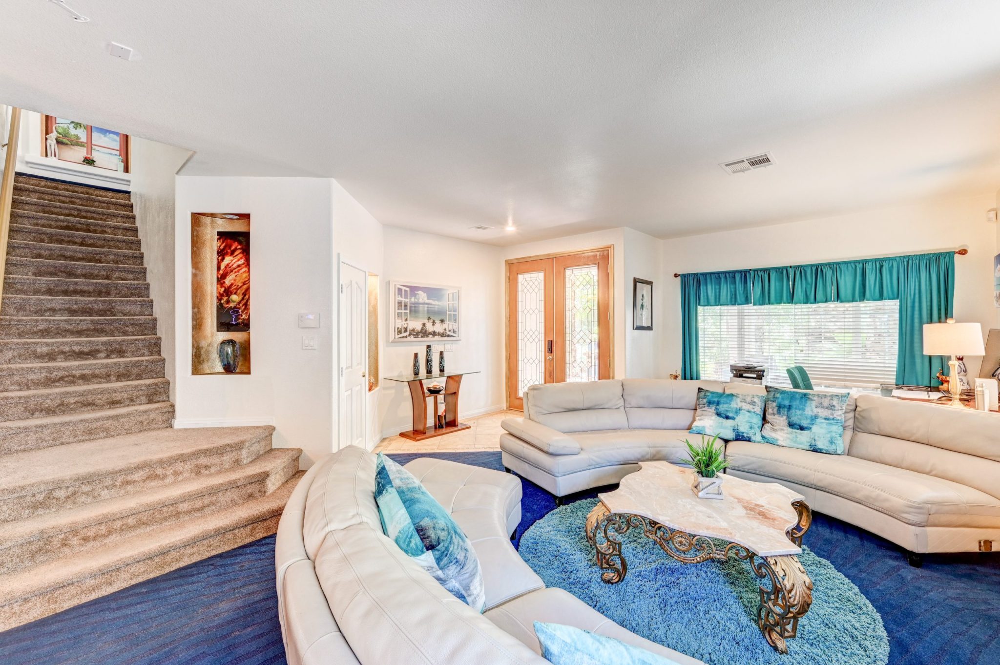 In Paradise Estate, a rental mansion in Vegas, a modern living room has two half-circle white couches ahead of a staircase going up, with white walls and blue floors and accents.