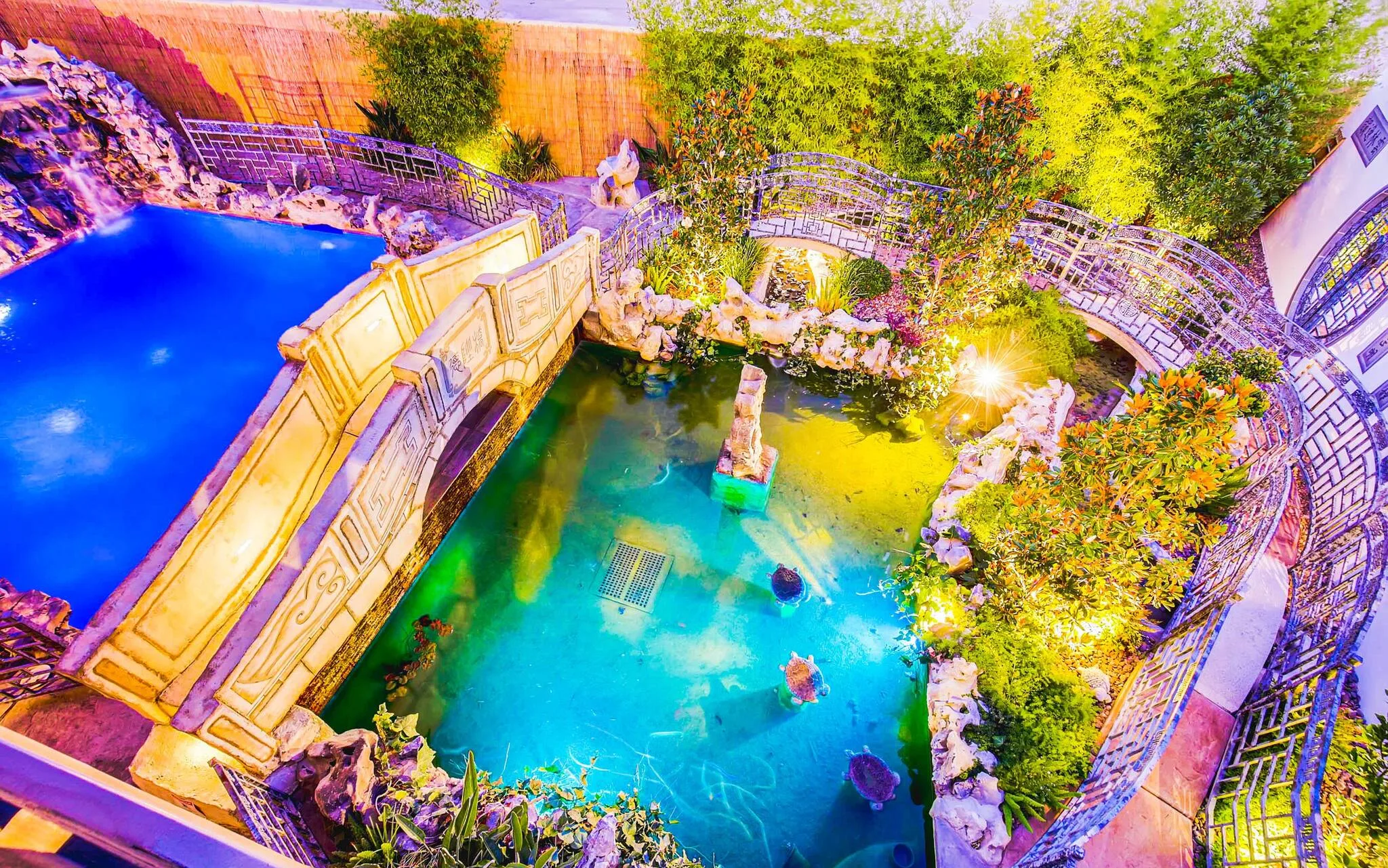 An elegant two-tiered pool is seen from above, with venetian-style stonework and greenery surrounding the bright blue pool waters in a luxury Vegas home called D&D Mansion.