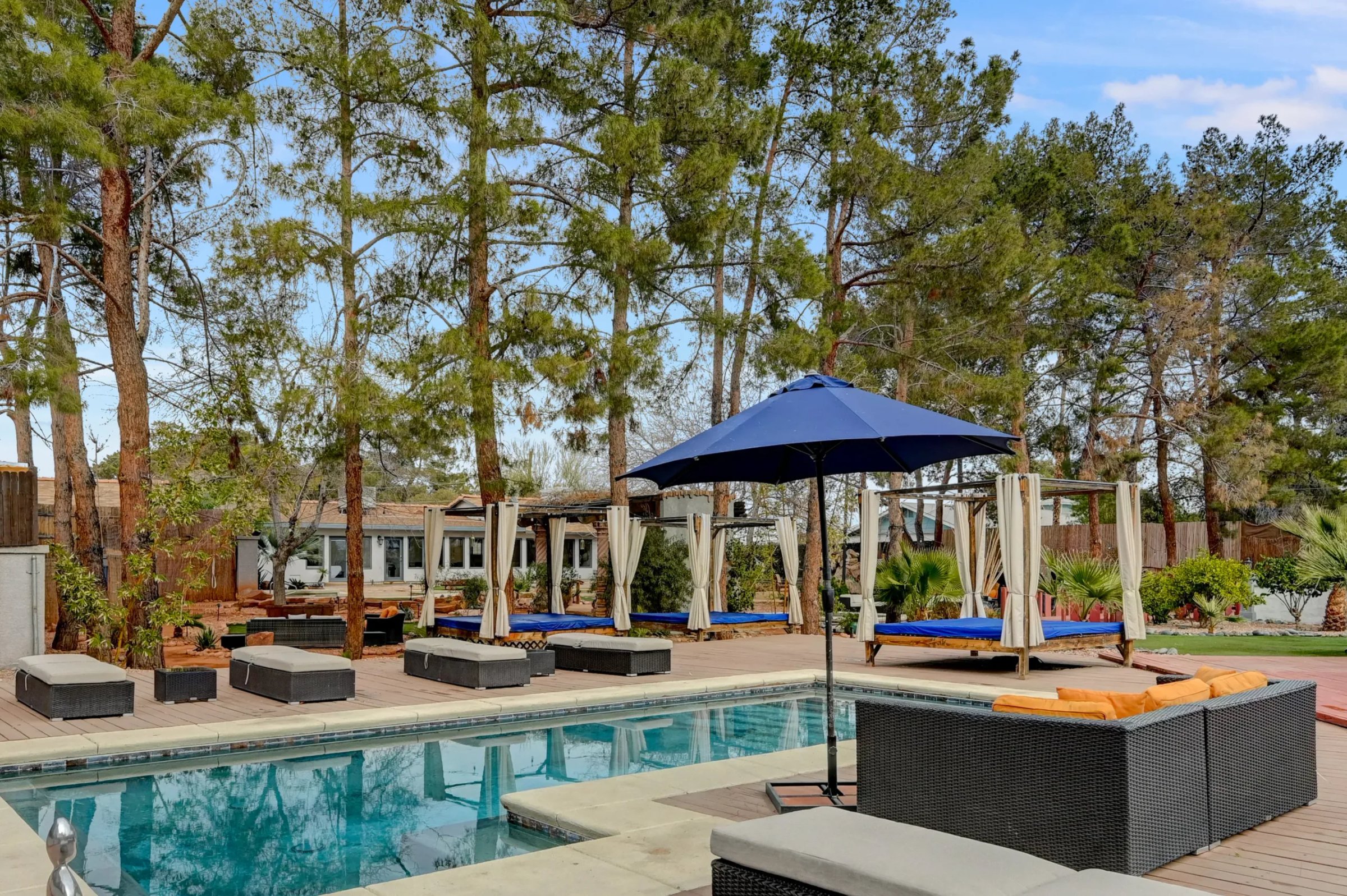 Loungers surround one of the pools in the backyard of Zen Paradise, a mansion rental in Las Vegas, with trees lining the back of the yard.