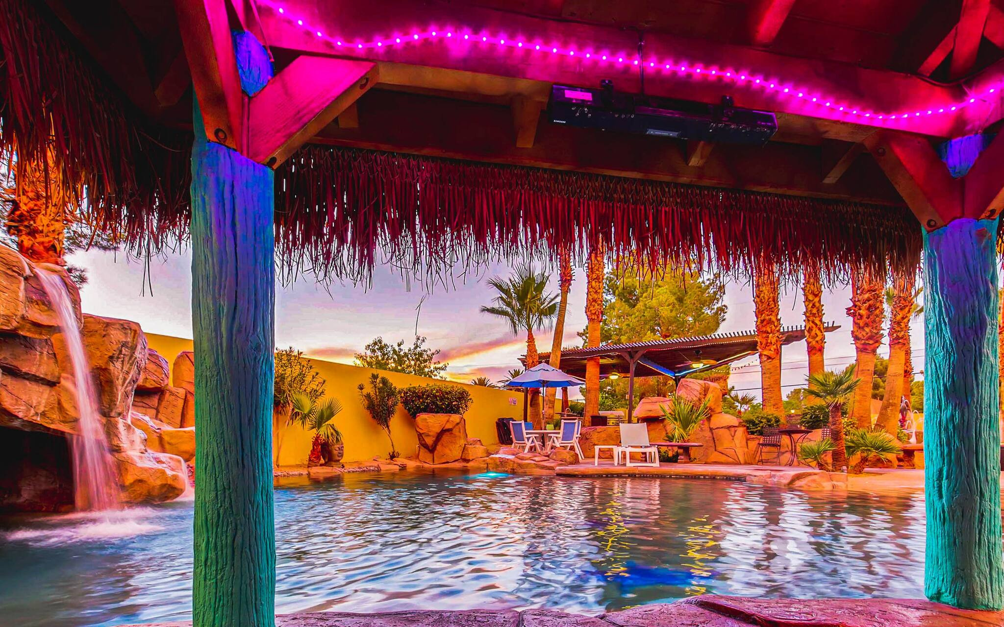 A resort-like pool featurng palapas, palm trees, a grotto and a waterfall, in the private setting of a rental mansion in Las Vegas.