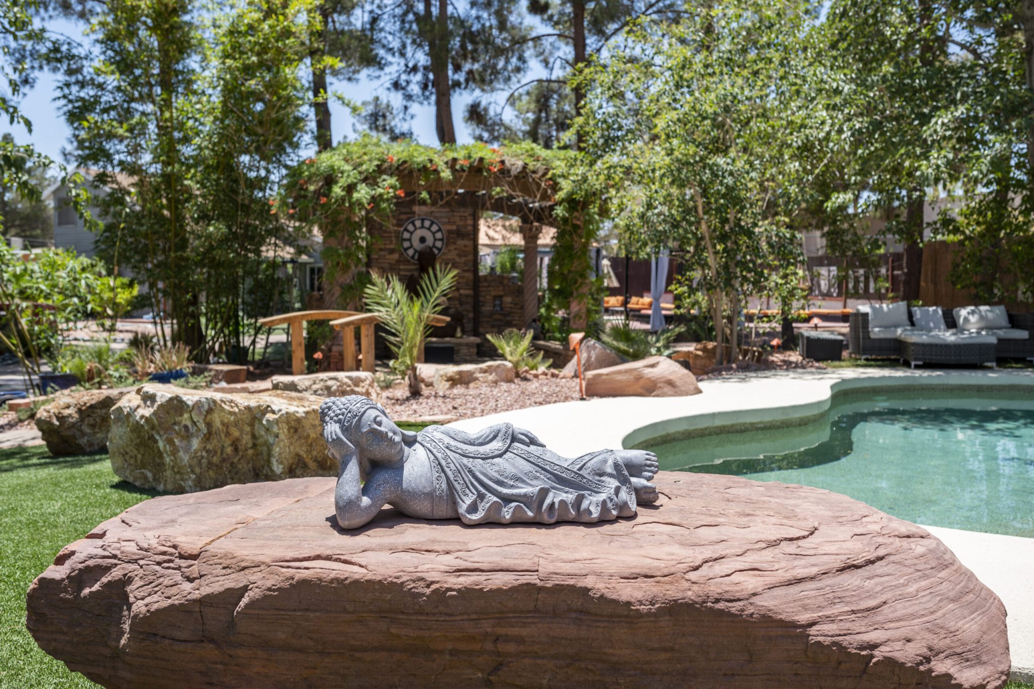 A relaxing garden in the backyard of a Vegas luxury mansion, with a pool and a buddha statue in the foreground.