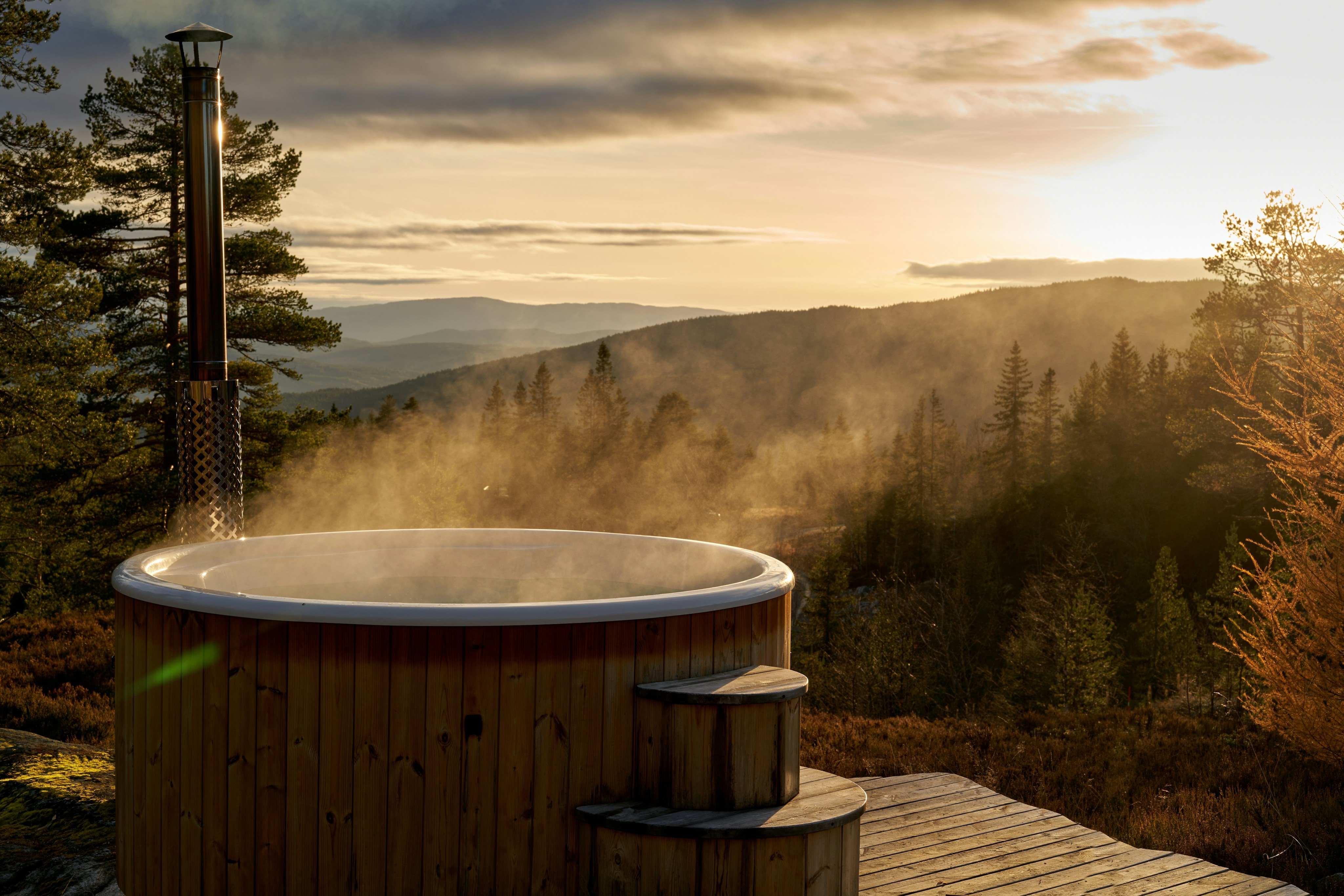 Steaming hot tub on a deck overlooking a forested valley at golden hour