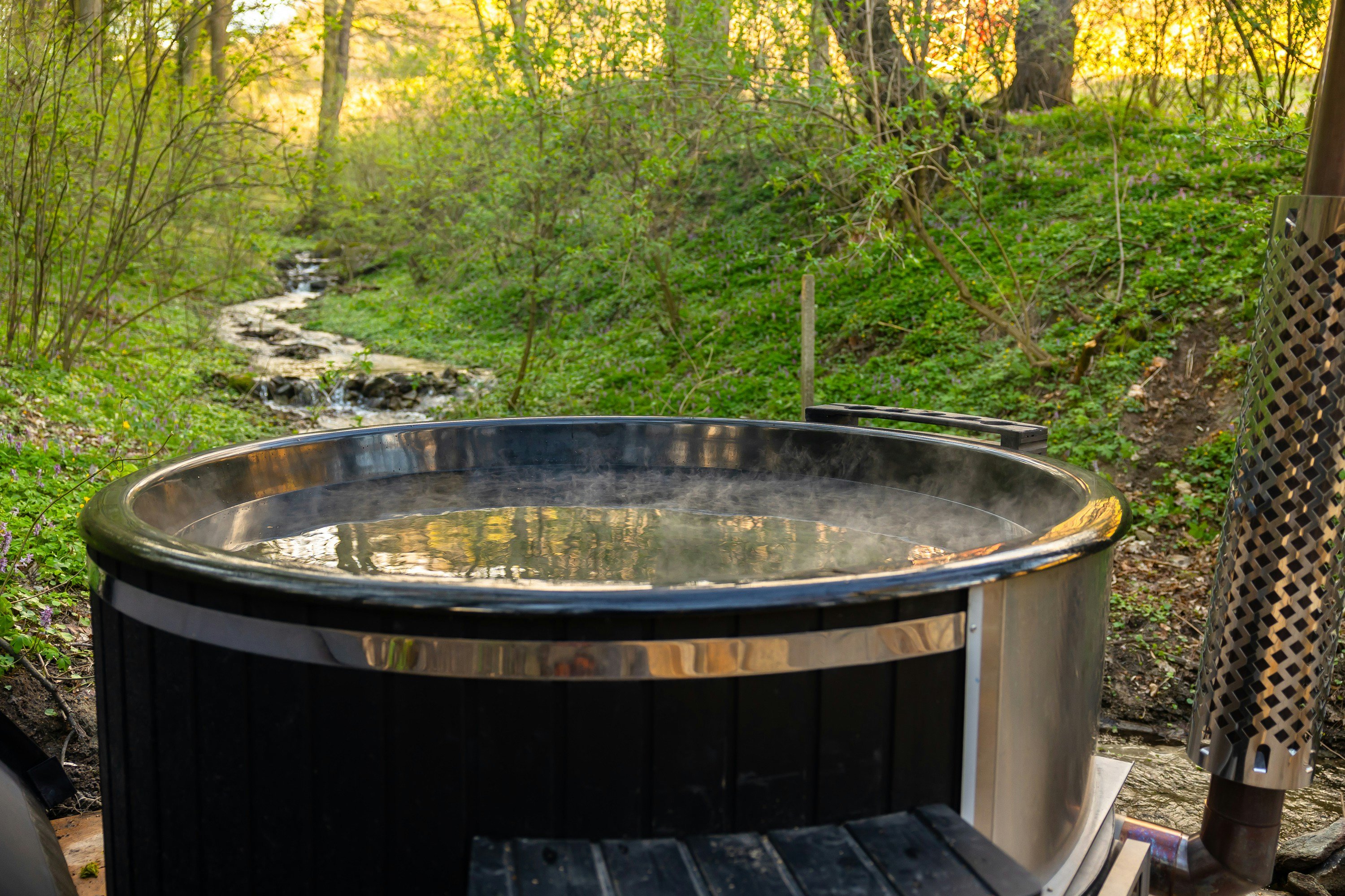 Outdoor hot tub steaming beside a forest creek in Hochatown