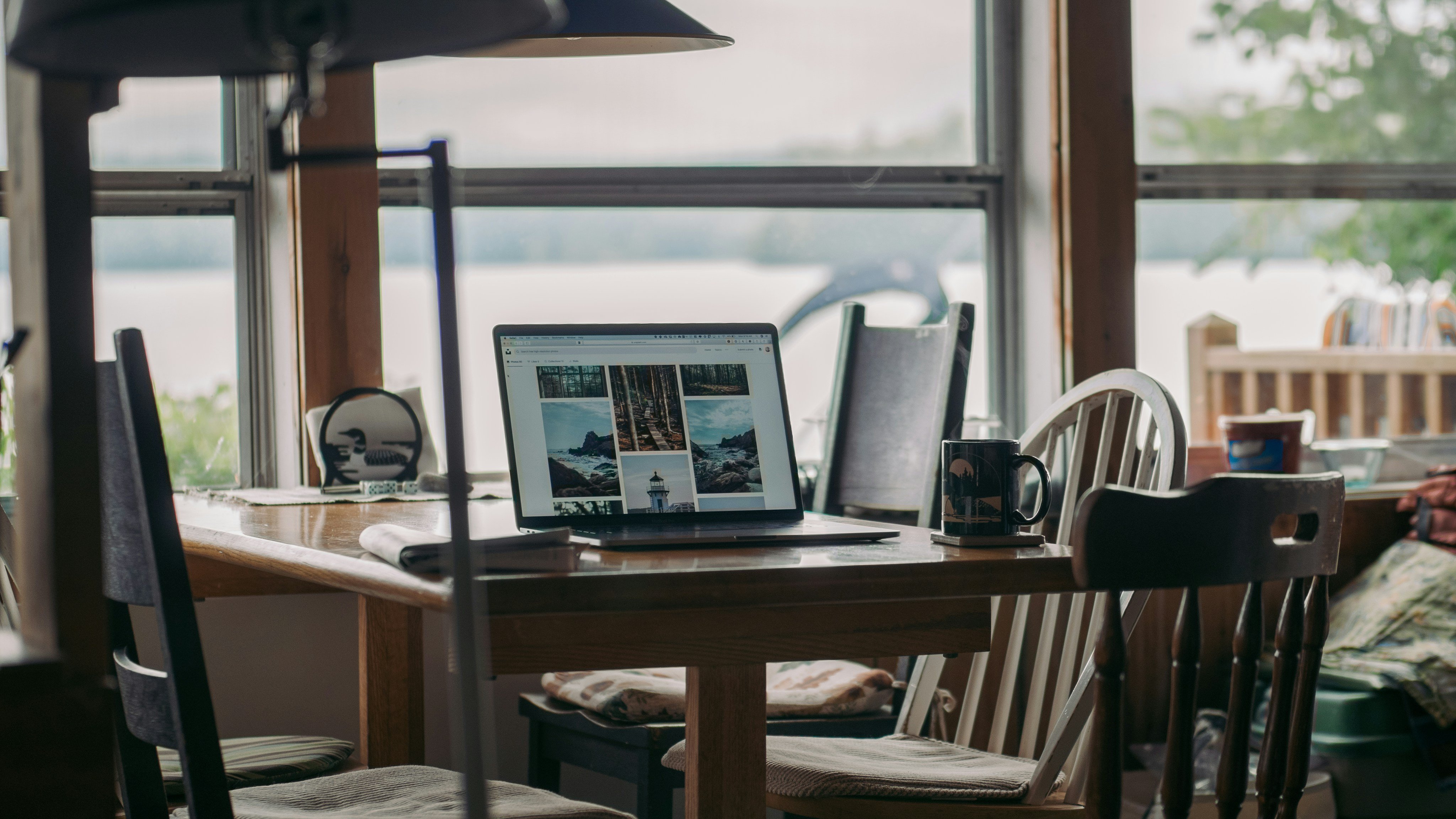 Laptop open on a rustic cabin table with lake view through the windows