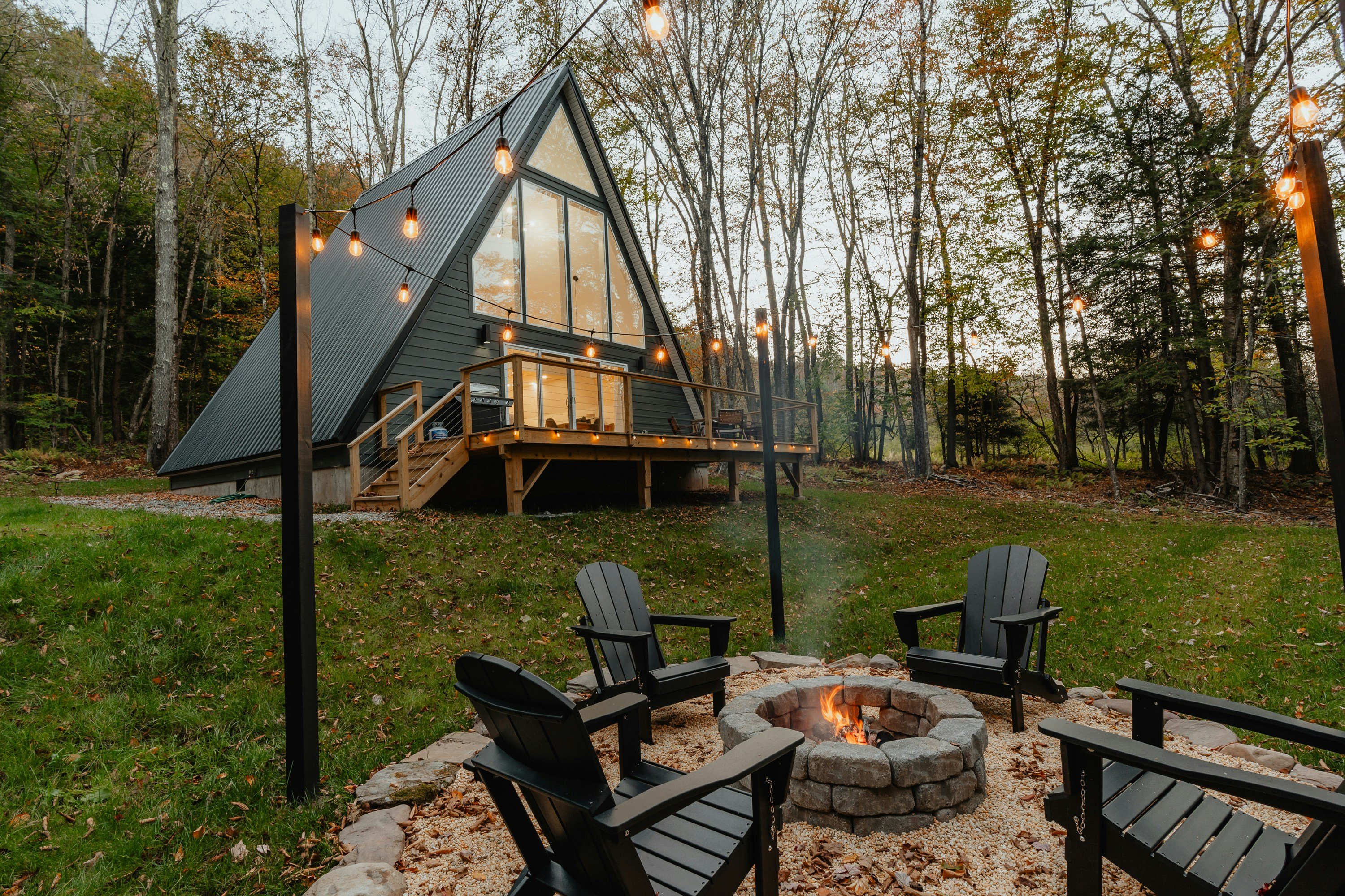 A-frame cabin with fire pit and string lights in autumn forest