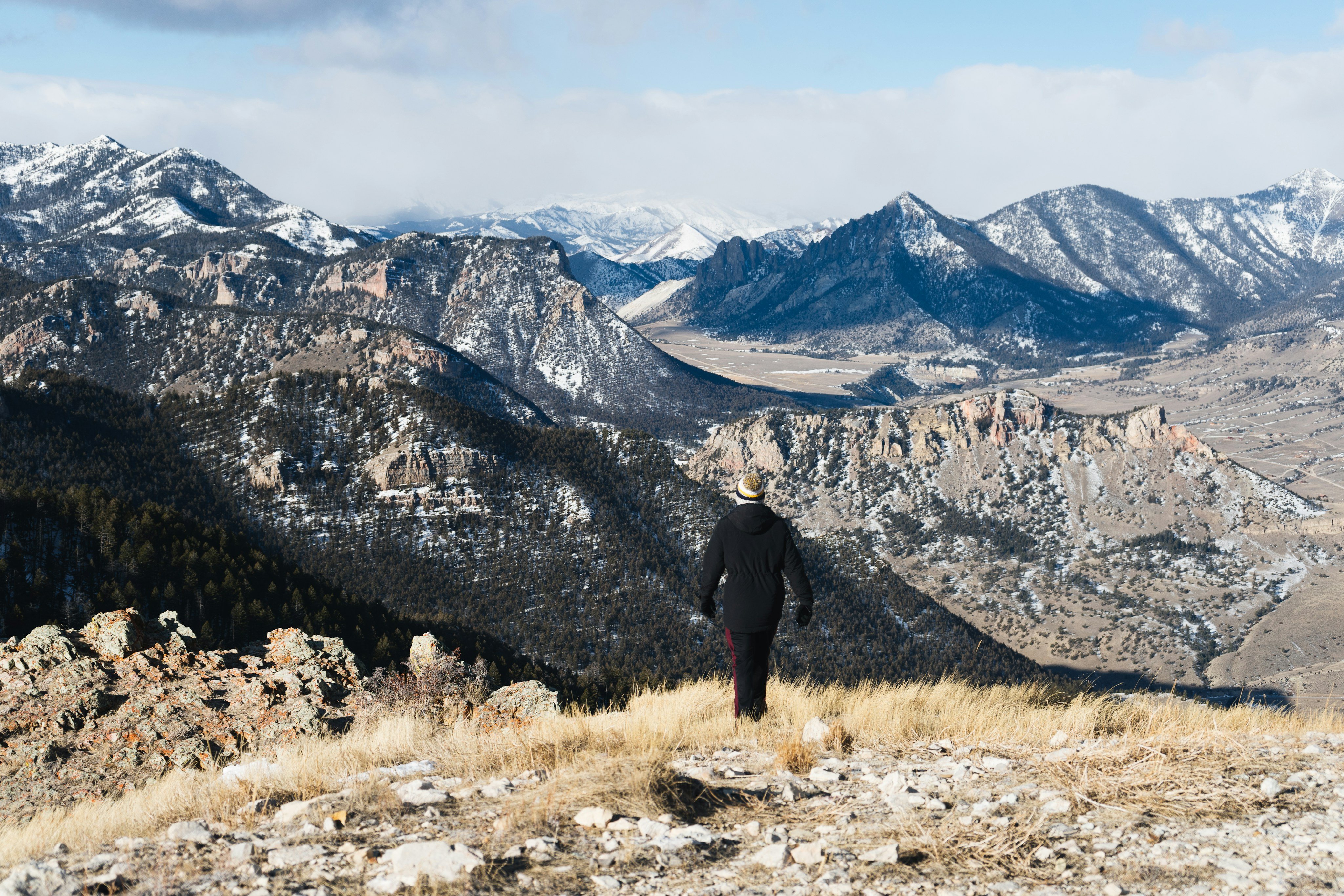 Lone figure on snow-dusted Wyoming ridge overlooking vast mountain range