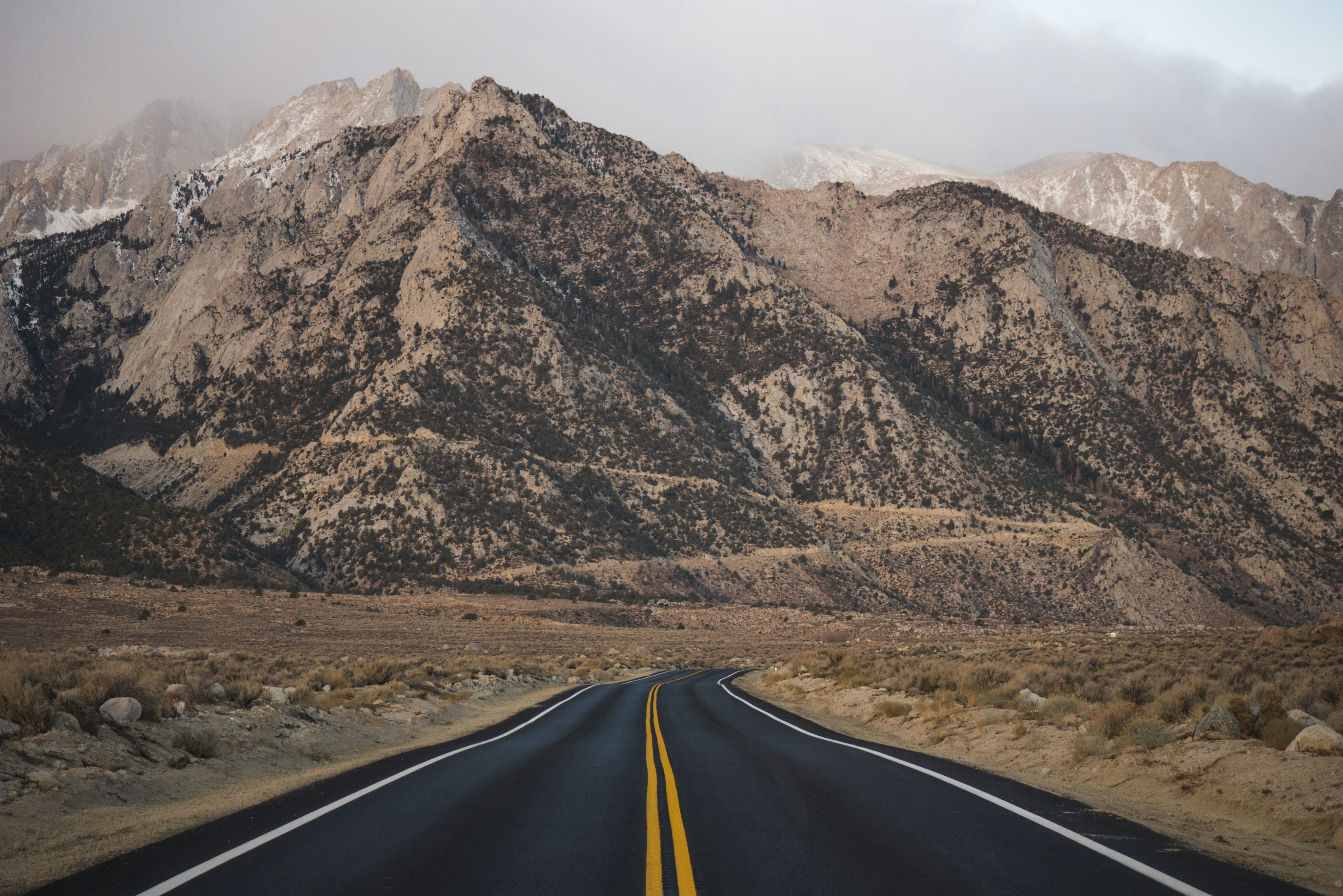 Empty two-lane road leading straight toward snow-capped mountains