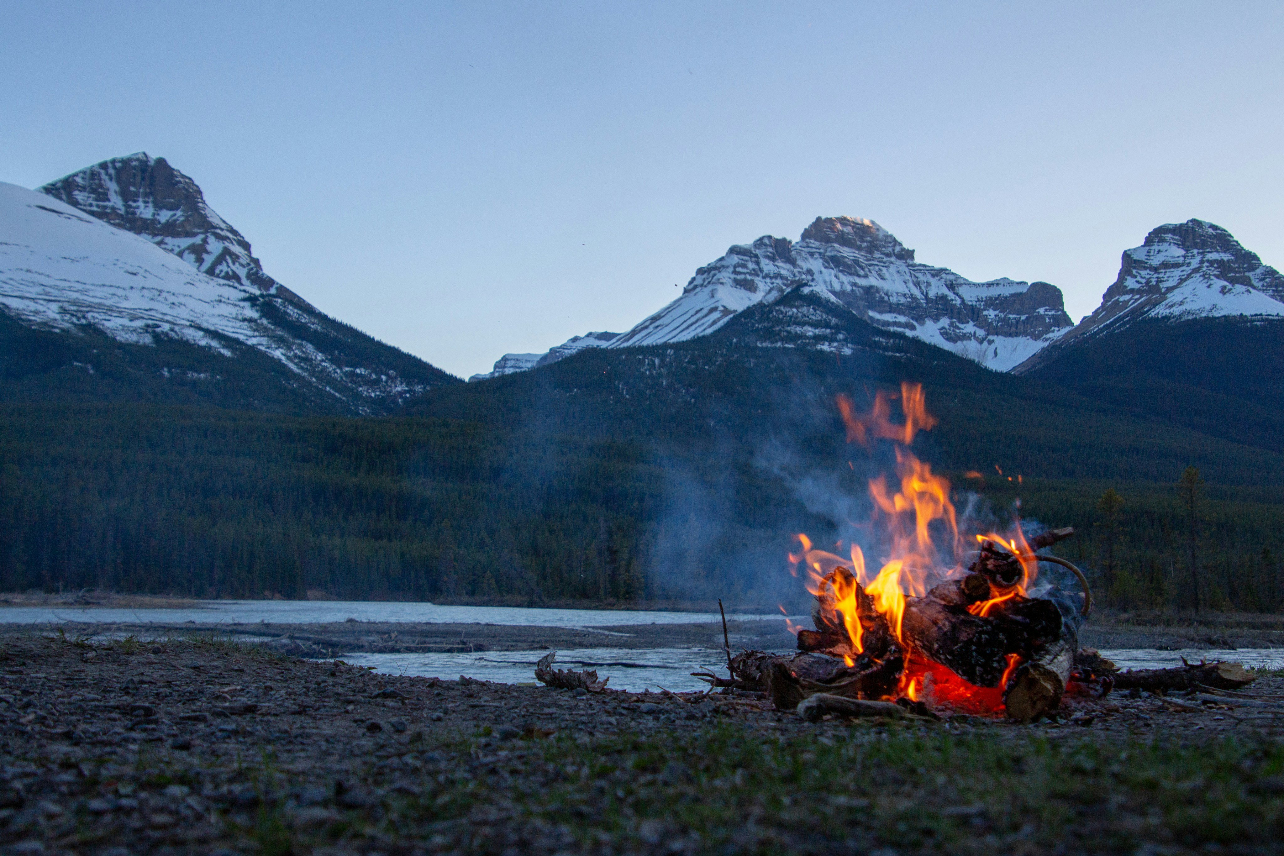 Campfire at dusk with snow-capped mountains in the background