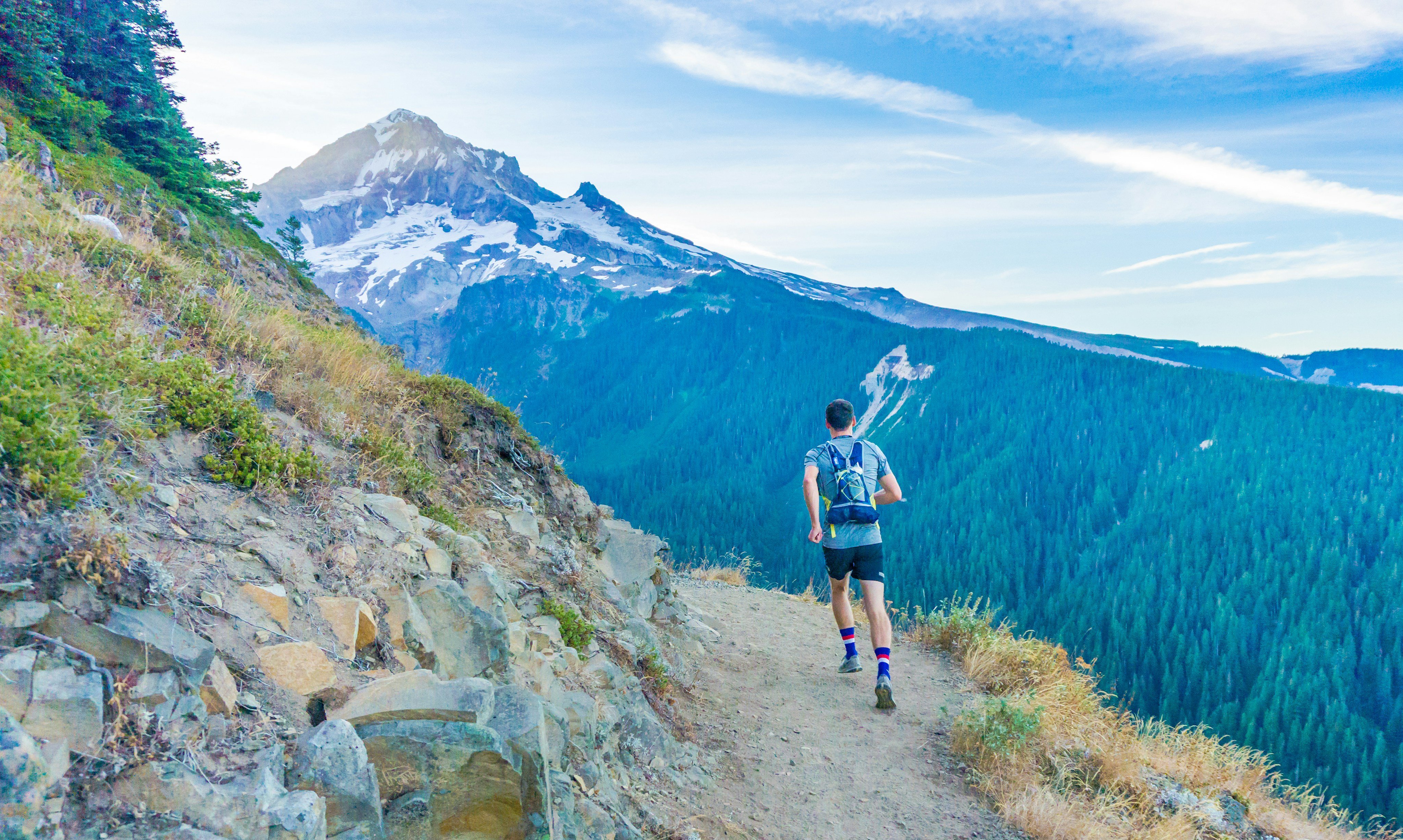 Trail runner on rocky single-track, snow-capped peak behind, Bighorn Mountains Wyoming