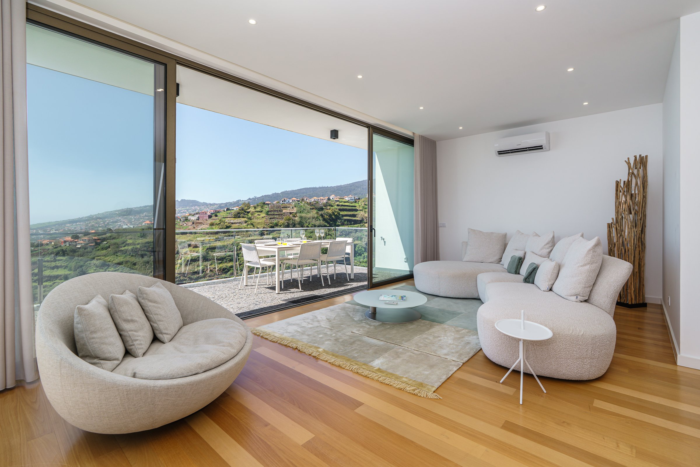 Bright living room in a contemporary Madeira villa with wide sliding doors, terrace dining area, and open views over the hillside.