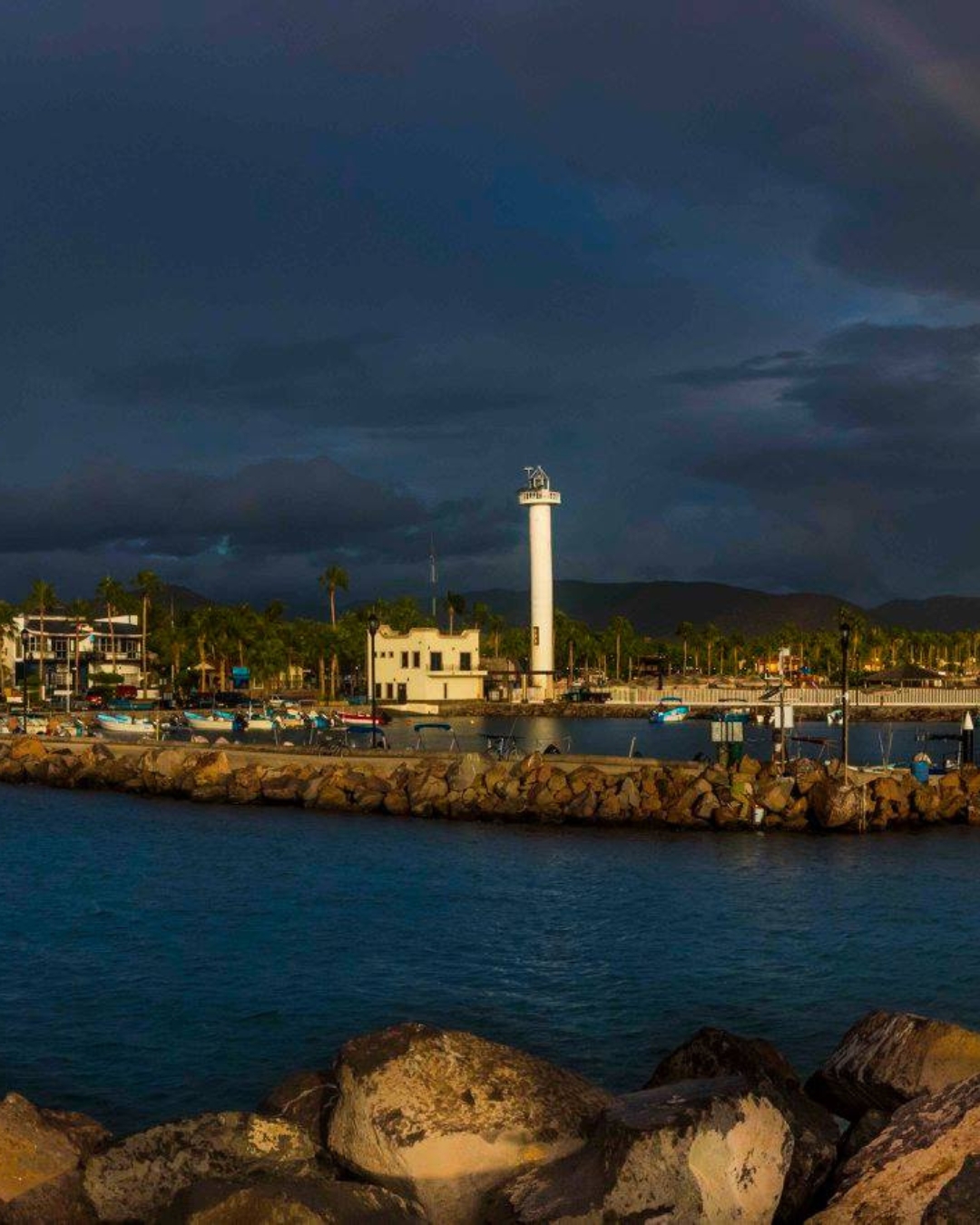 Loreto lighthouse and marina at dusk, with fishing boats along the stone breakwater