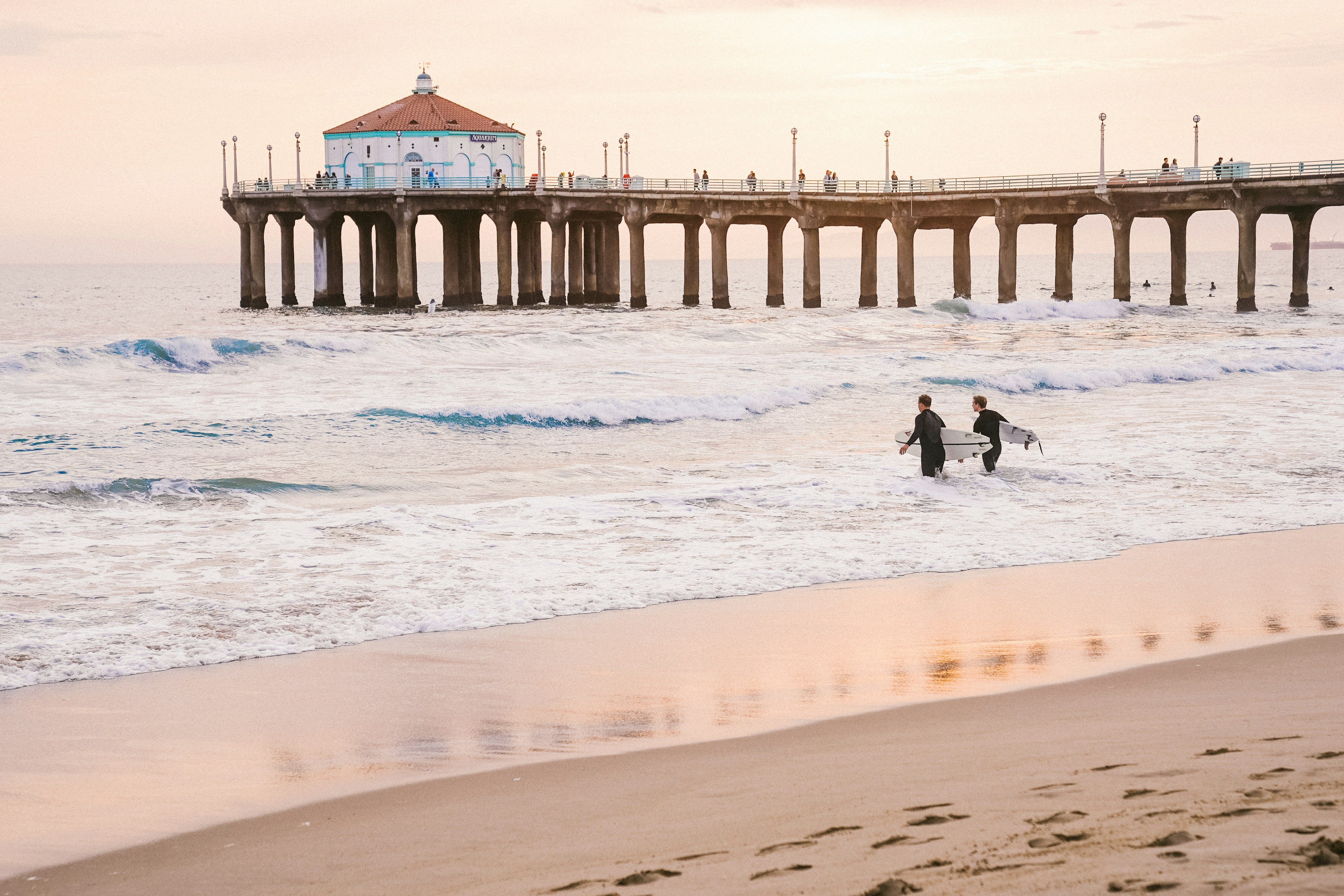 Manhattan Beach pier at golden hour, two surfers walking in the shallows