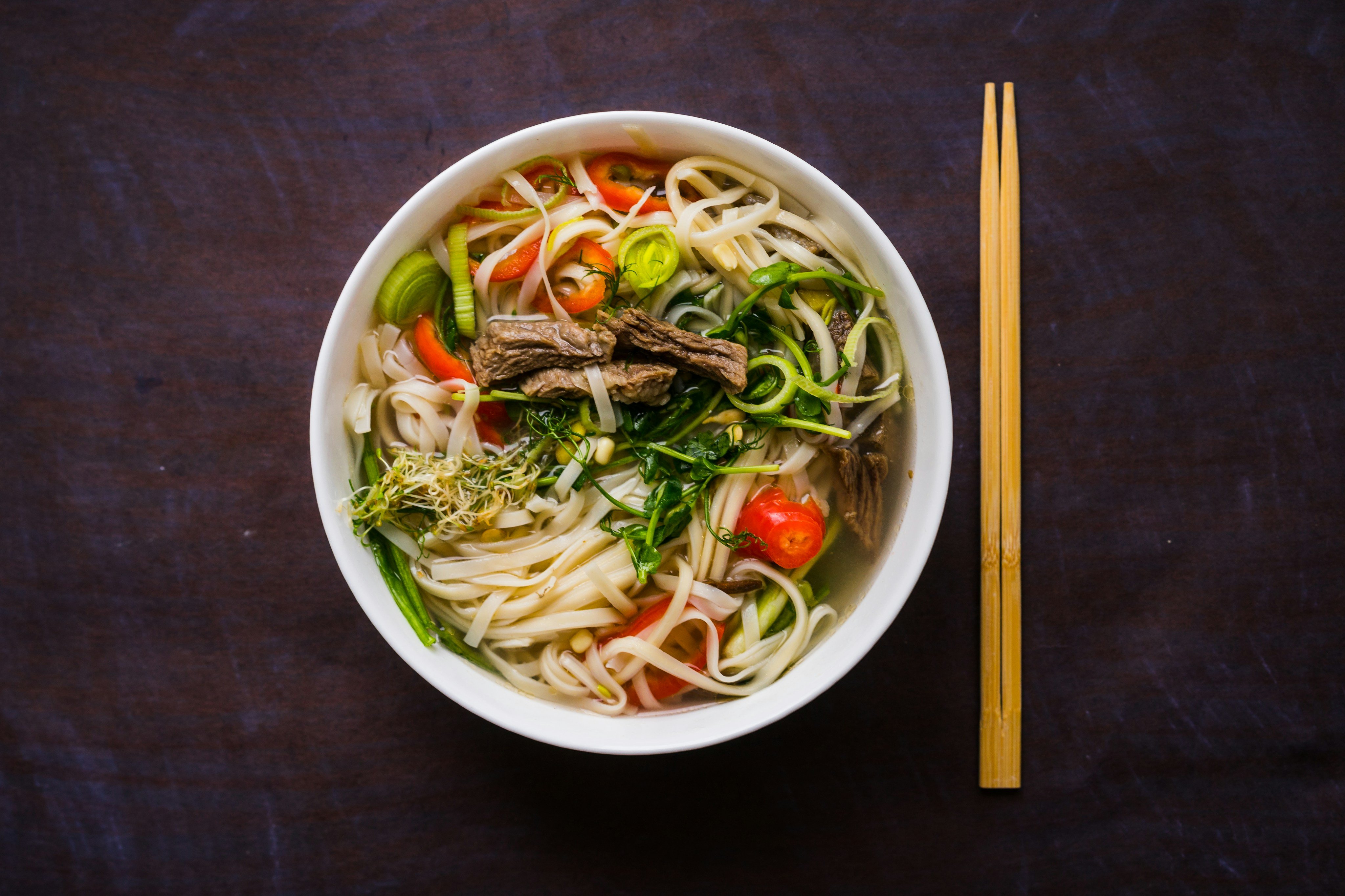 A bowl of pho bo with fresh herbs, noodles and chopsticks
