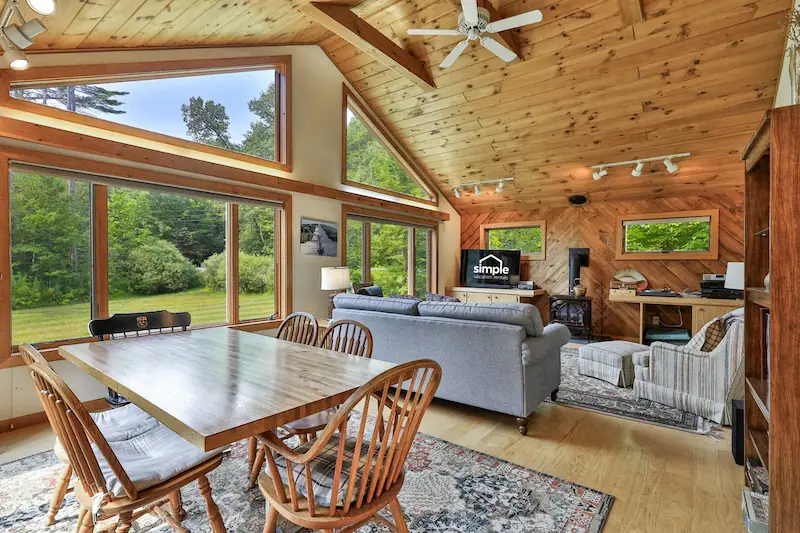 Warm Vermont cabin interior with wood finishes and large windows overlooking the forest.
