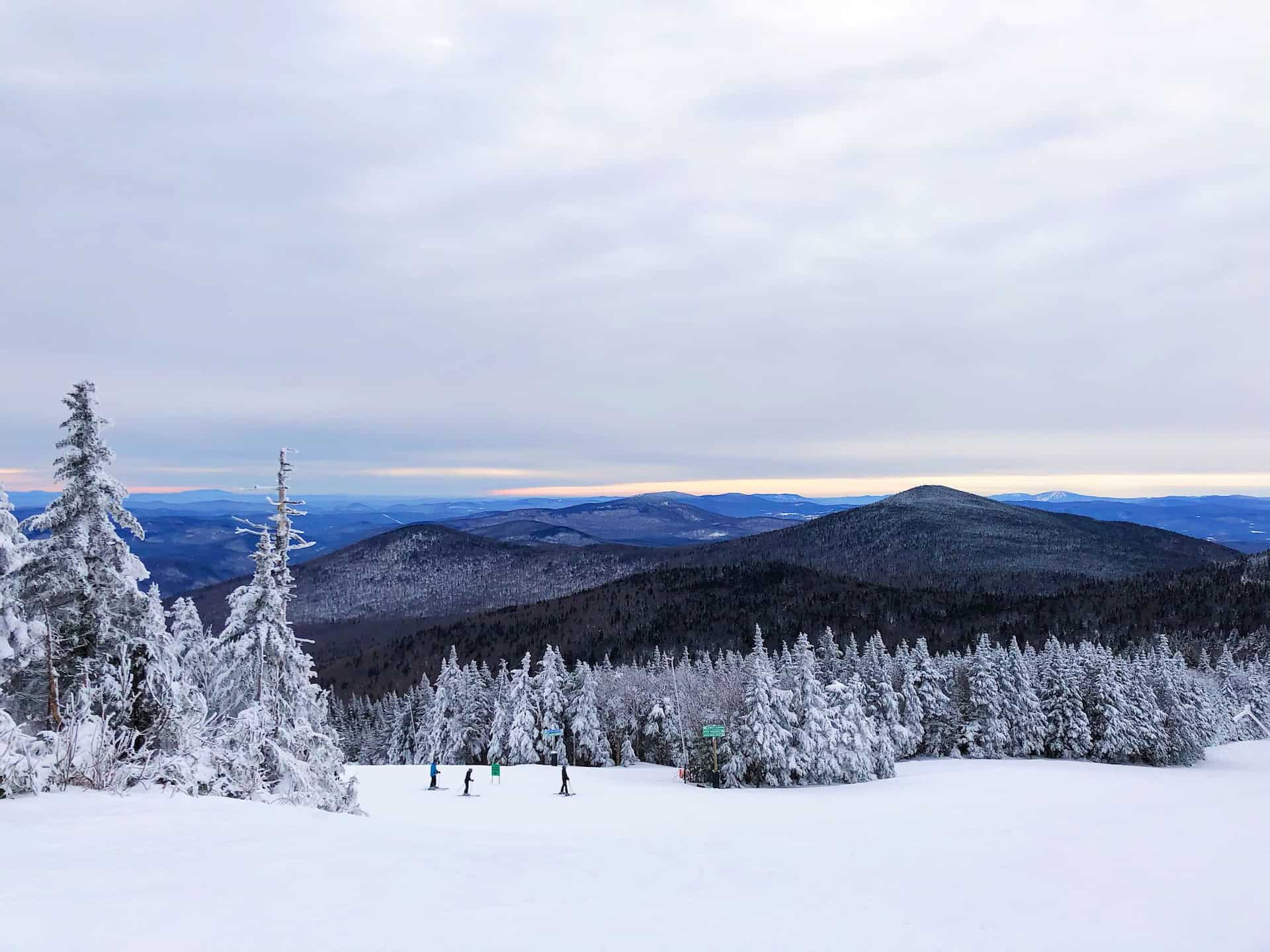 Panorama of Killington Mountain, with a few people skiing near many snowy trees.