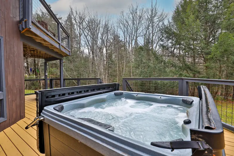 Deck of a Vermont vacation cabin with a hot tub and a view of birch trees.