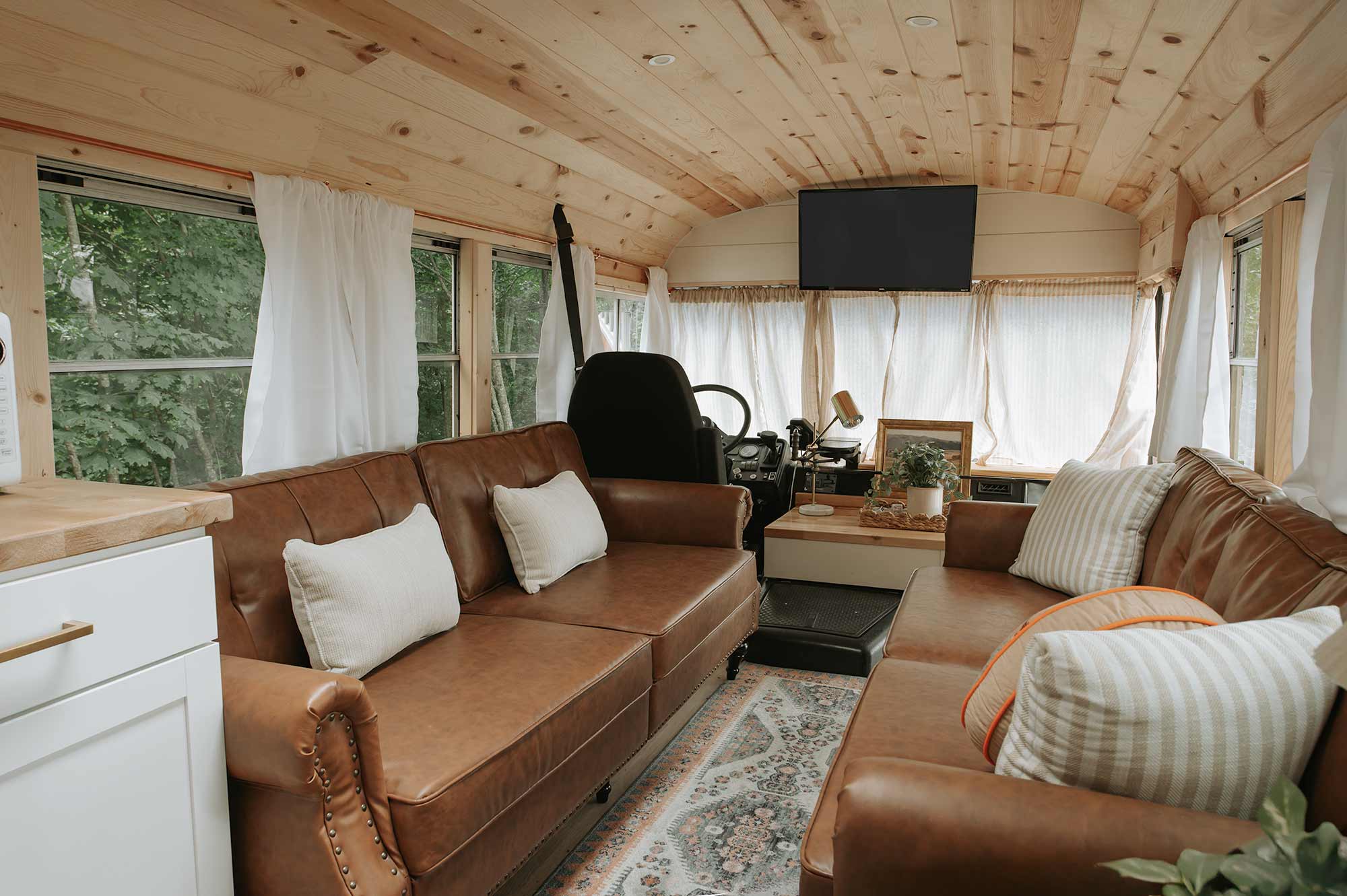 Interior of Snuggle Bus skoolie rental in Tennessee with leather couches, cozy pillows, and wood-paneled ceiling, designed for comfort and Instagram appeal.