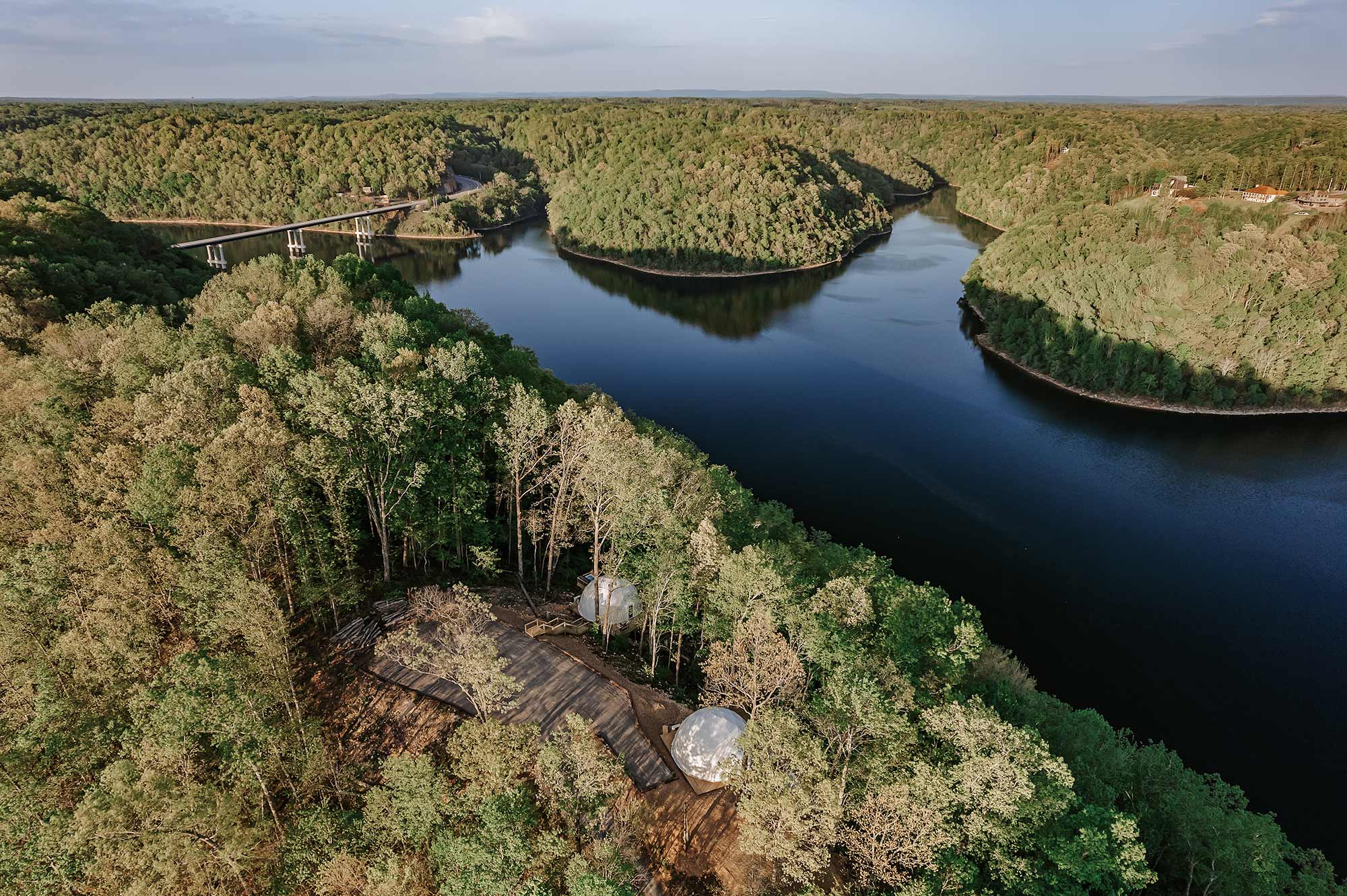 Aerial view of Center Hill Lake surrounded by forested hills, with glamping domes tucked into the trees near the shoreline, an ideal fishing getaway in Tennessee.