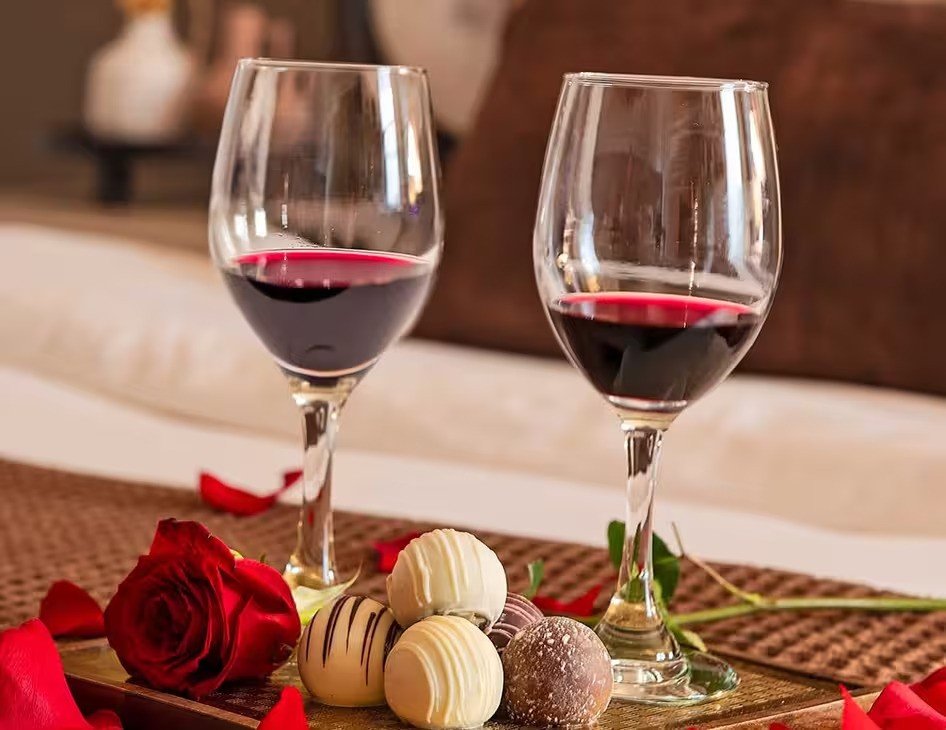 Two glasses of red wine with chocolate truffles and a rose on a tray