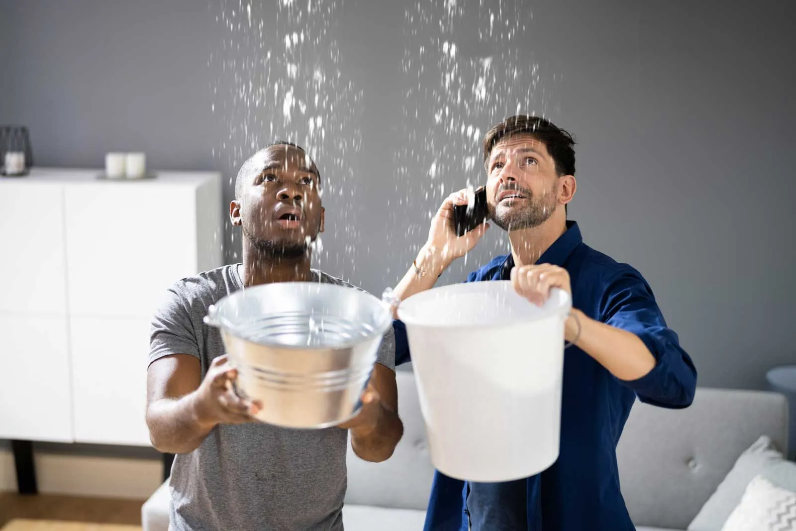 two men holding buckets as water drips from above